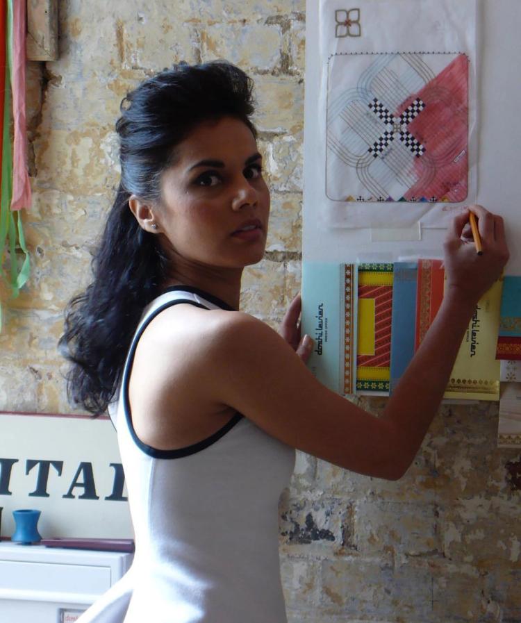 Nipa Doshi facing the camera whilst holding a pen against a drawing up against a brick wall.