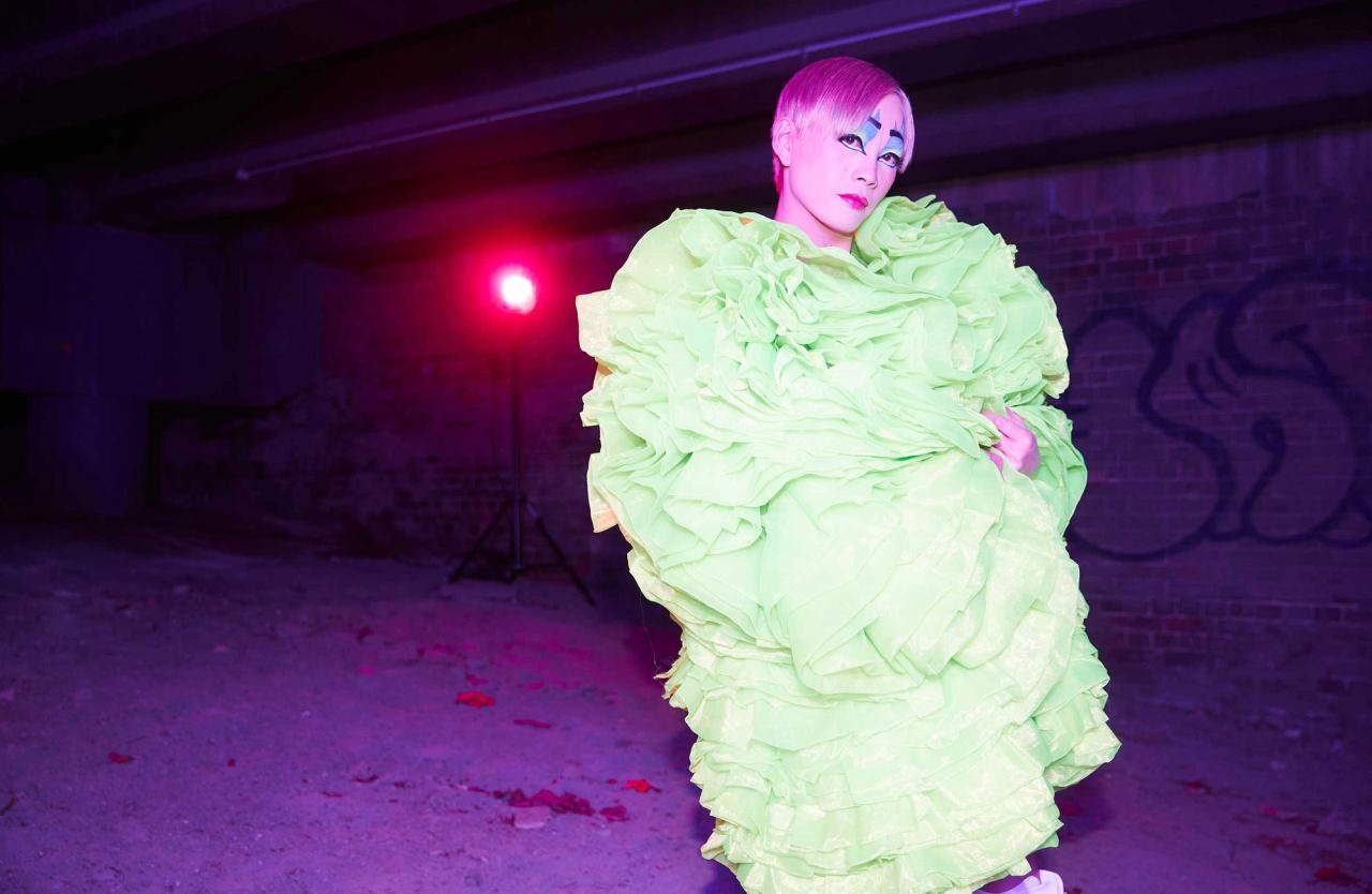 Figure posing in green ruffles and purple light behind them