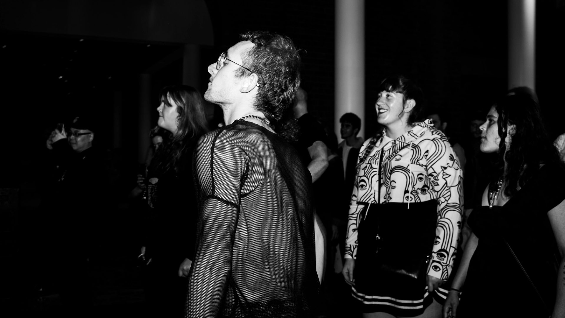 Black and white image of person in netted shirt in a crowd