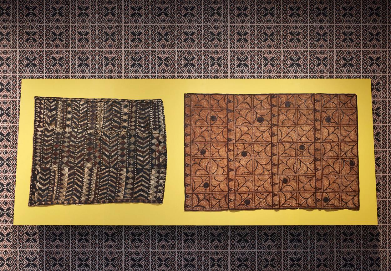 Two siapo (Sāmoan bark cloth) mounted on a wall, covered in a siapo-inspired wallpaper.