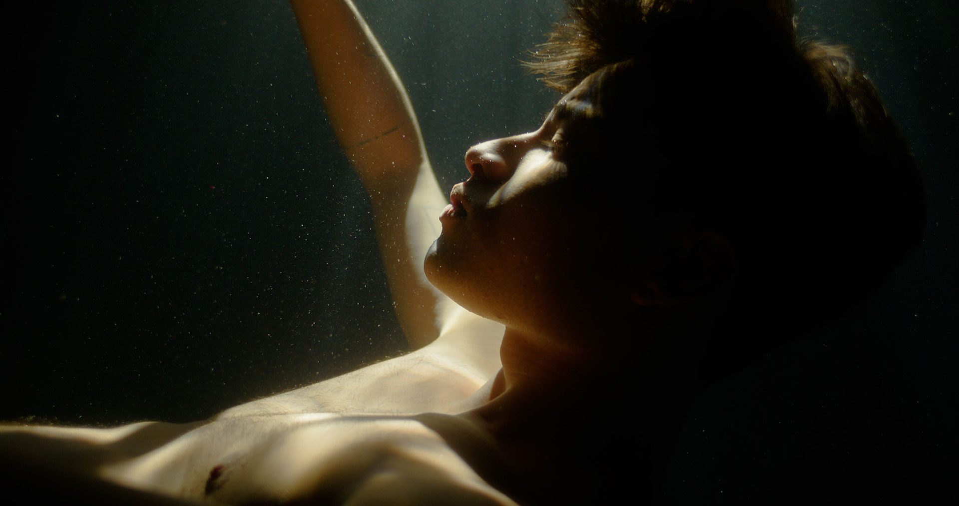Young adult underwater with light on their face with their eyes closed