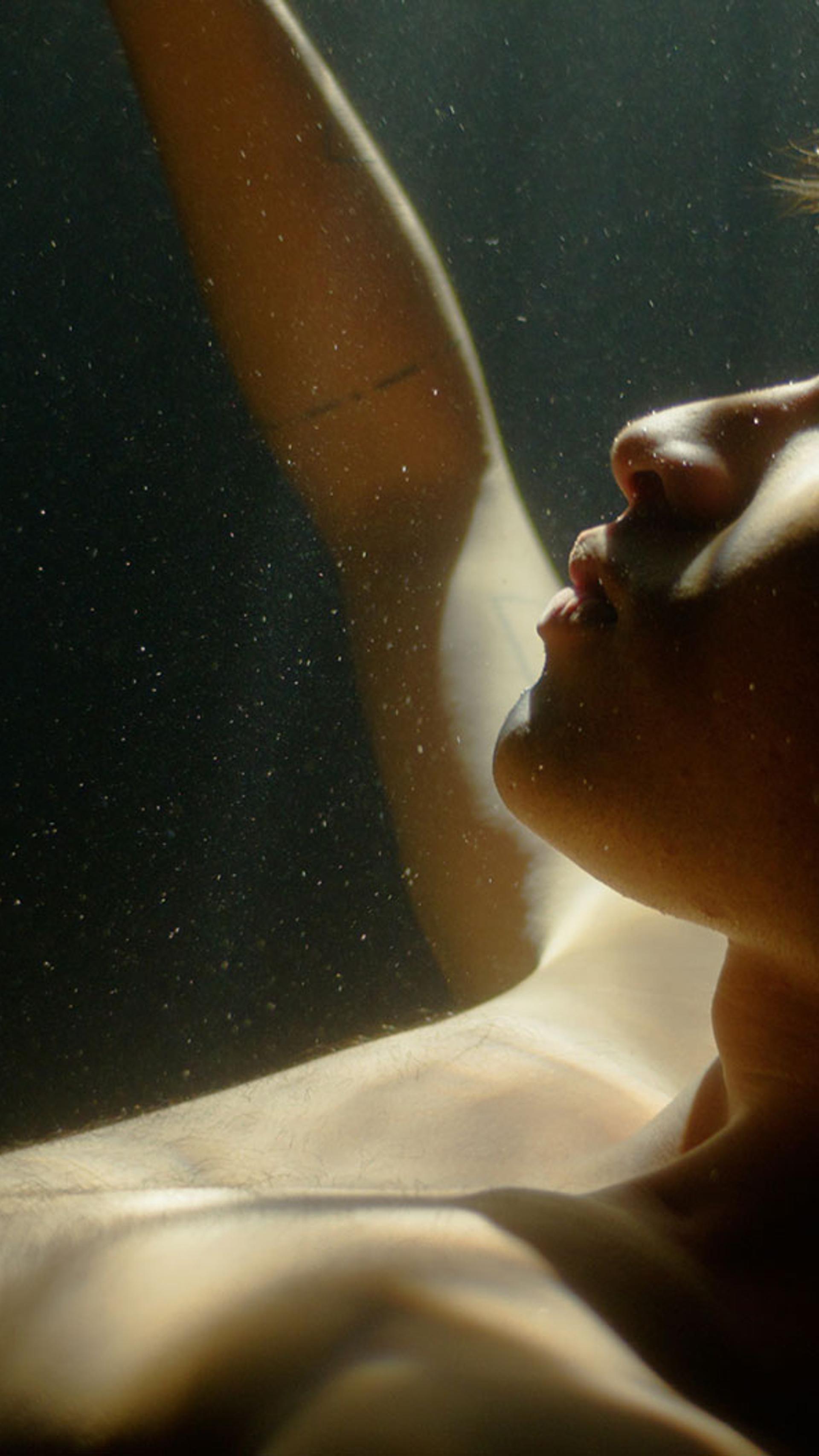 Young adult underwater with light on their face with their eyes closed