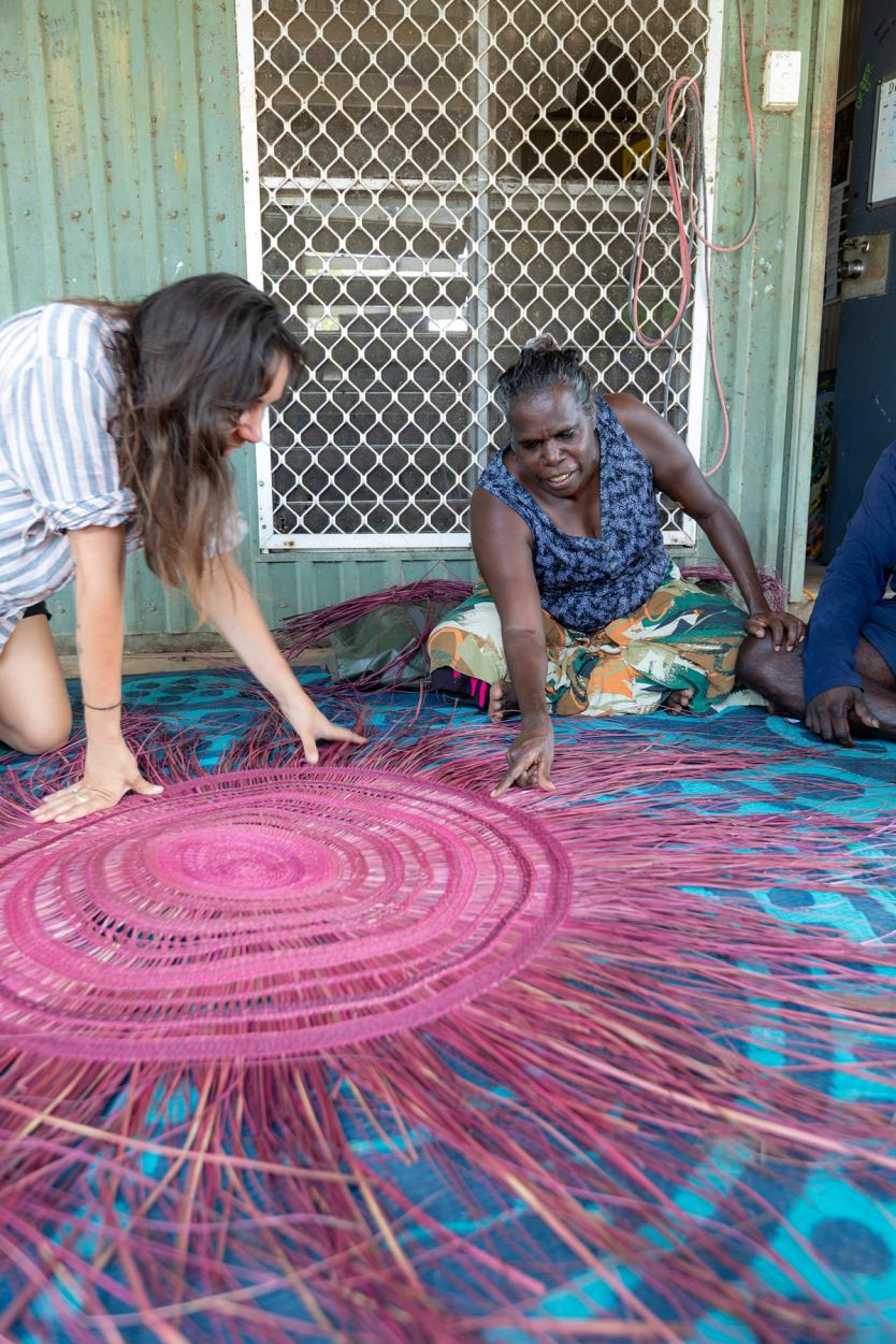 Women touching a traditionally woven mat on atop fabric on the floor