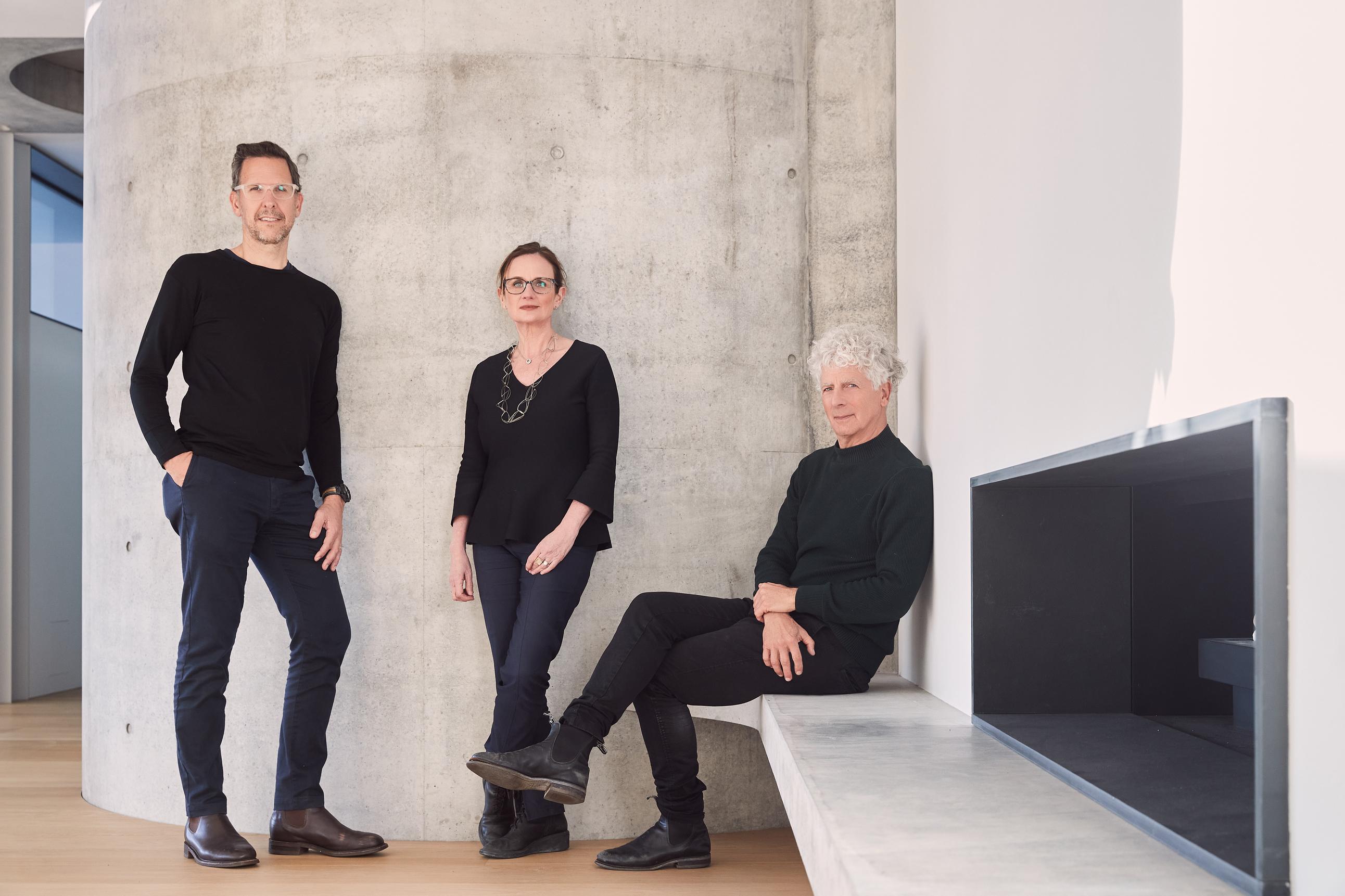 Three humans are posing for the camera inside an area with concrete backdrop.