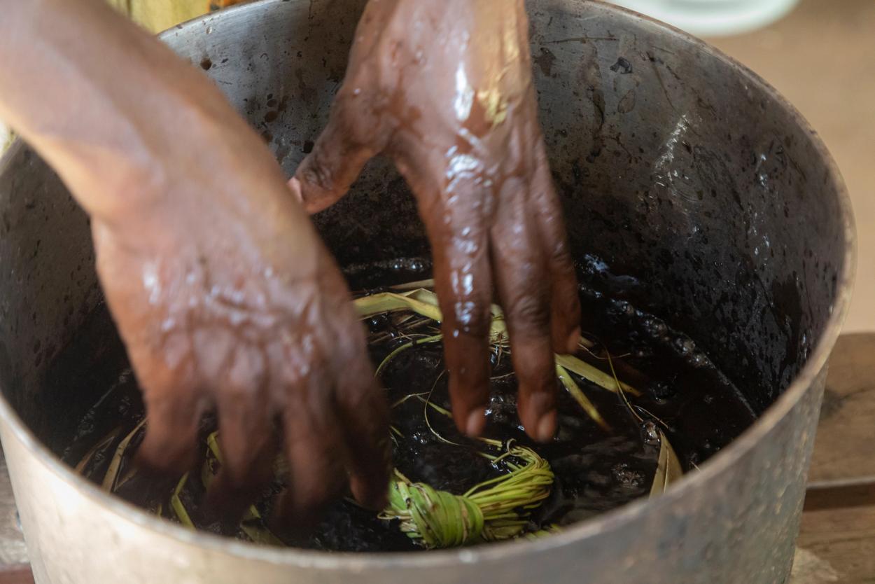 A woman’s hands reaching into a tin pot filled with pandanus and water.