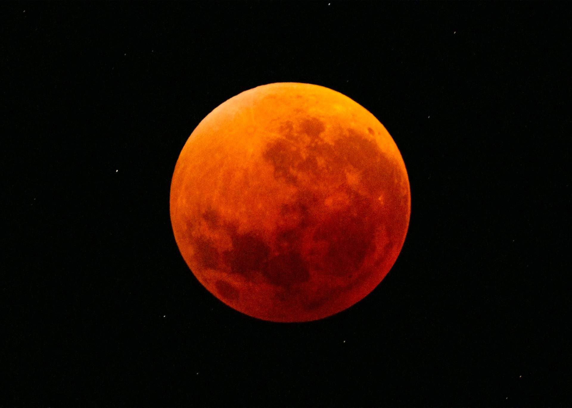 Total lunar eclipse showing the Moon fully immersed in Earth's shadow, appearing deep orange-red (blood moon) with visible surface details and a starry black background.
