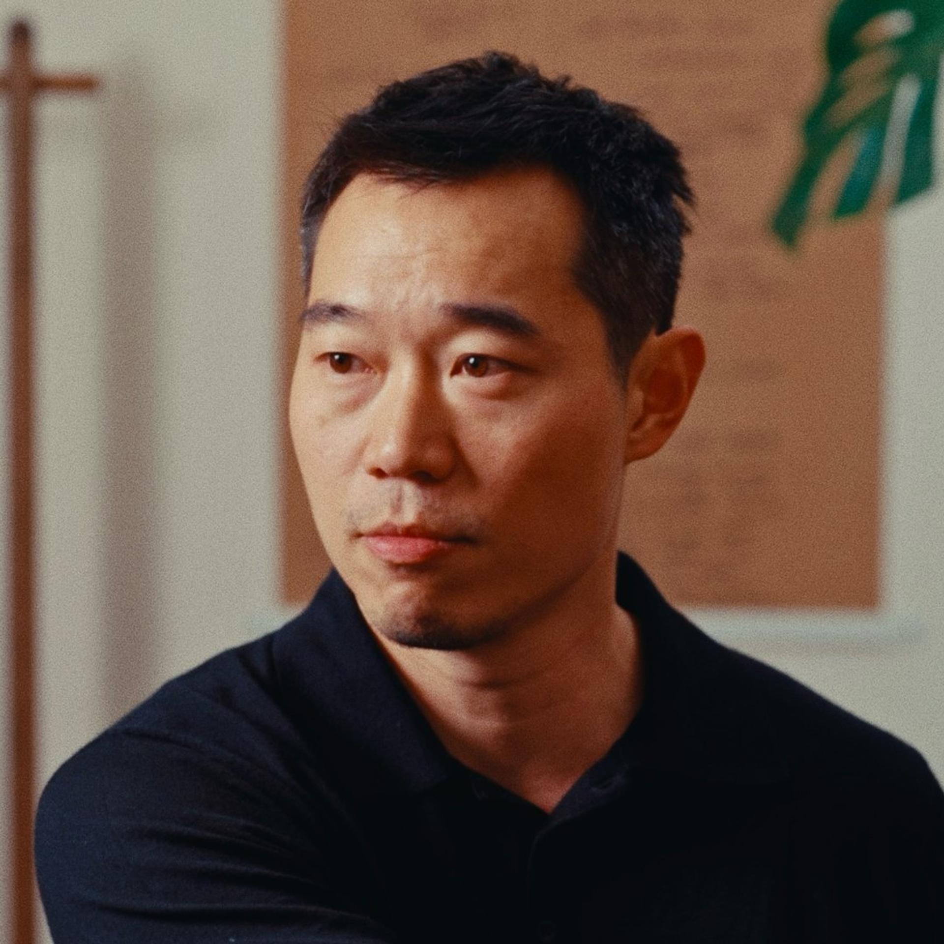 A close-up portrait of a man (Ken Sakata) with short black hair and looking to his right, away from the camera.