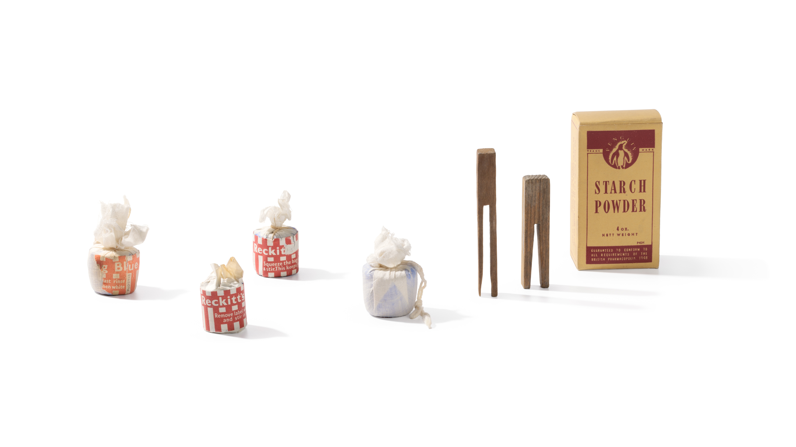 Photograph of laundry equipment consisting of four 'Reckitt's Bag Blue', one box of 'Penguin Starch Powder', and two handmade clothes pegs against a white background.