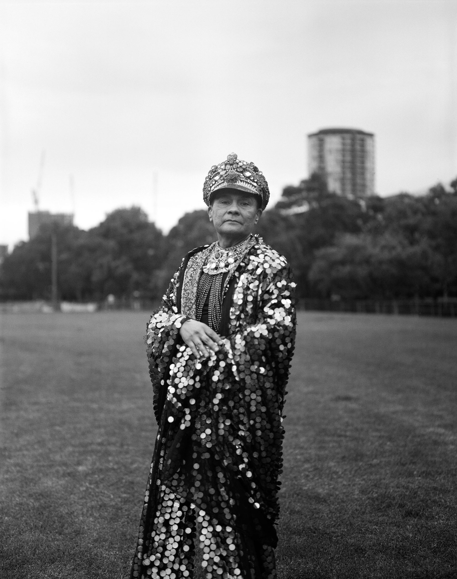 A black and white photo of a man standing on an oval. He is wearing a bejewelled hat and robe.