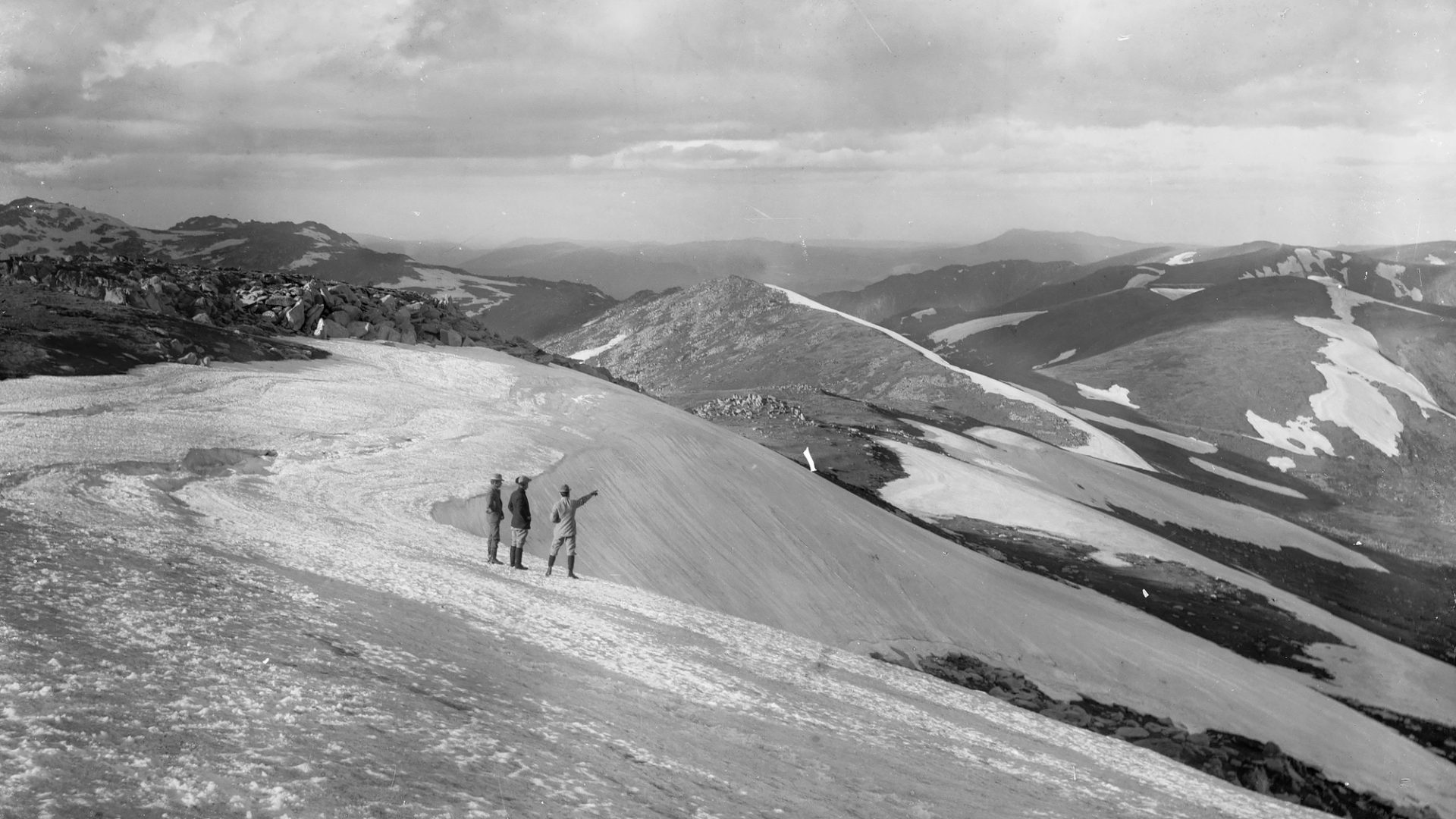 Far away humans in the snow mountains pointing away from camera