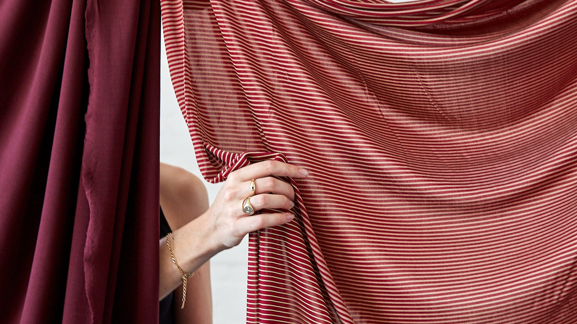 Two red fabrics clipped and hanging from a string with hands lifting and touching the fabric.