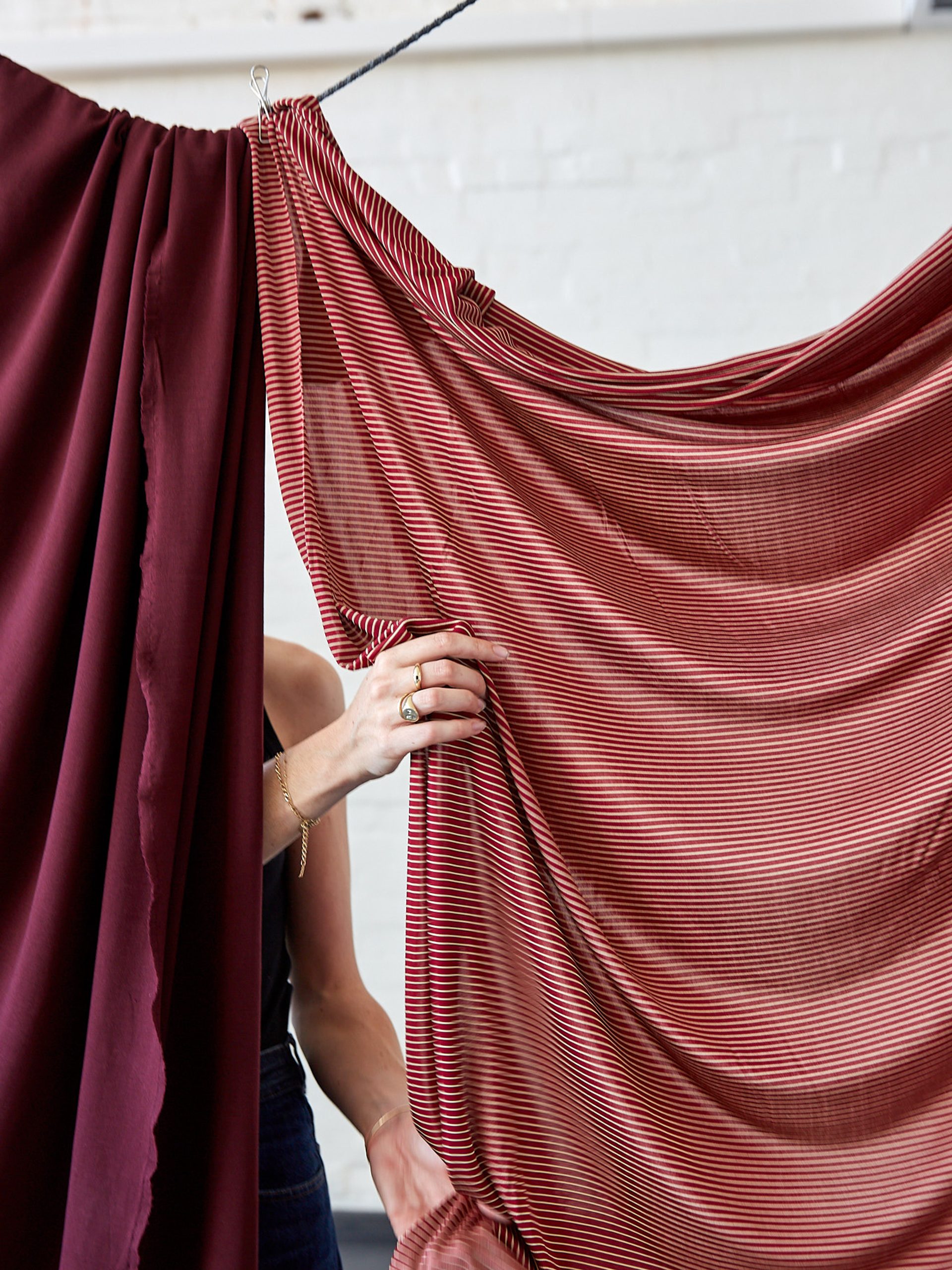 Two red fabrics clipped and hanging from a string with hands lifting and touching the fabric.