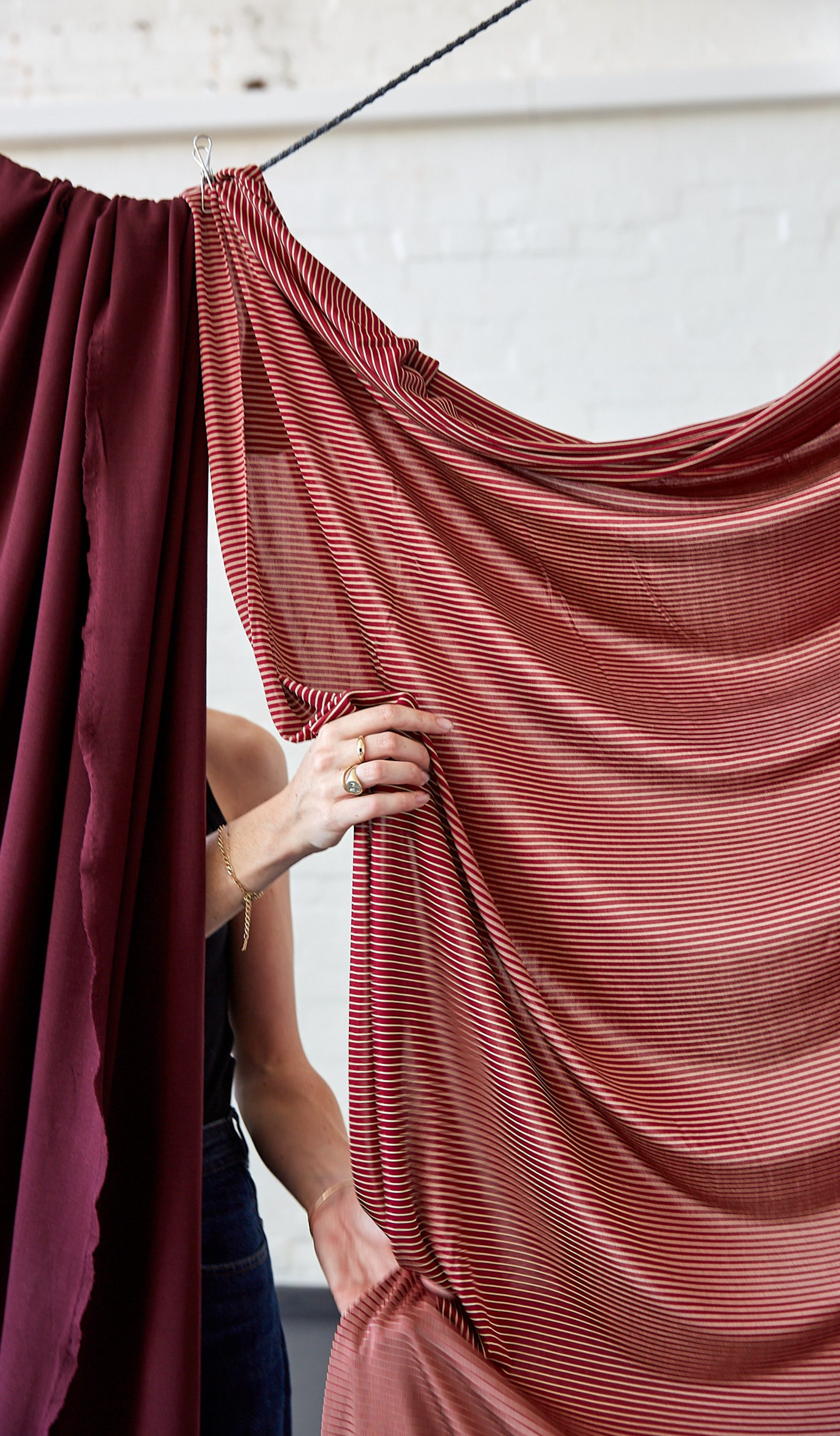 Two red fabrics clipped and hanging from a string with hands lifting and touching the fabric.