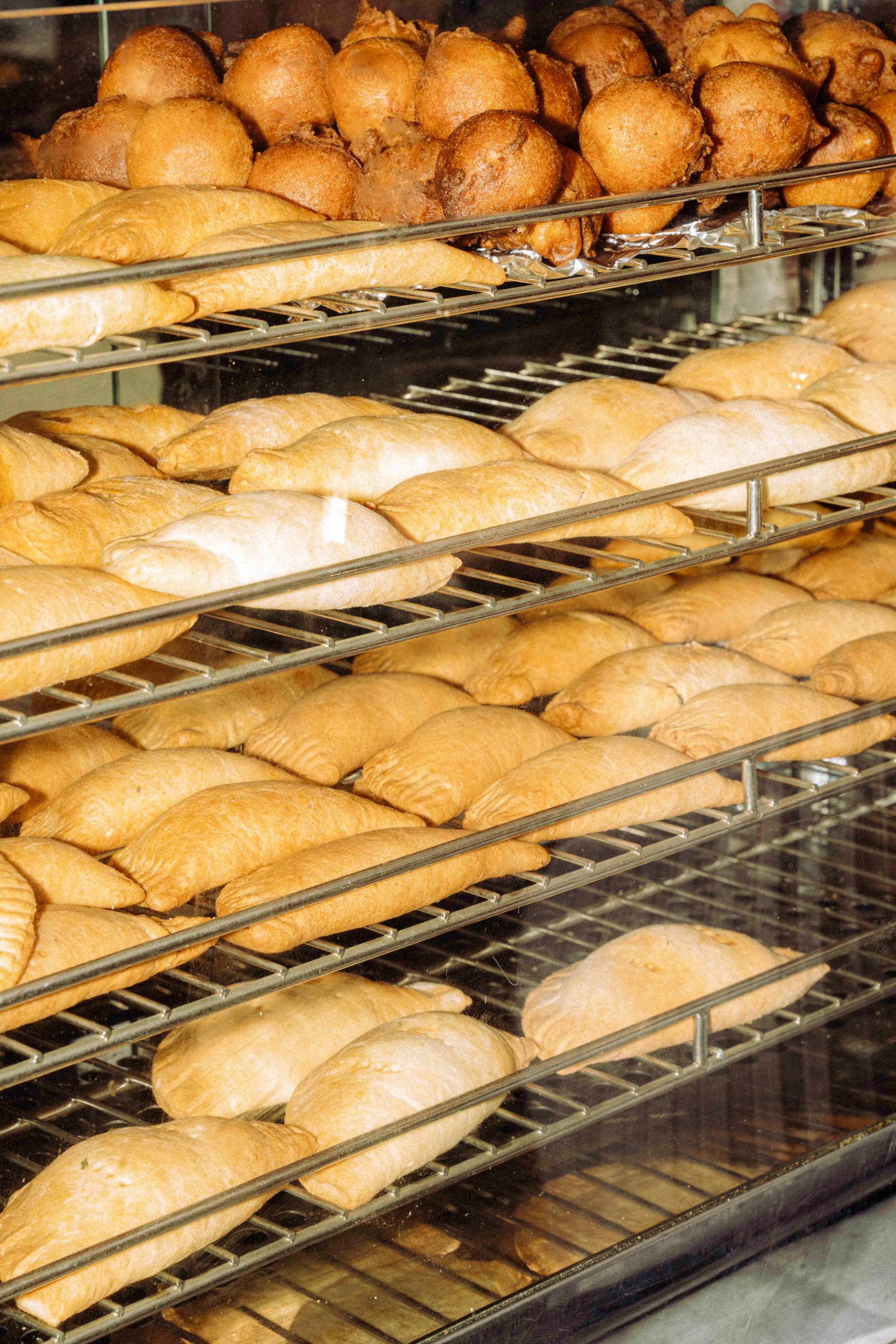 A display case filled with four neat rows of golden brown pastries and fritters, with deep-fried balls at the top and flatter pastries along the bottom.