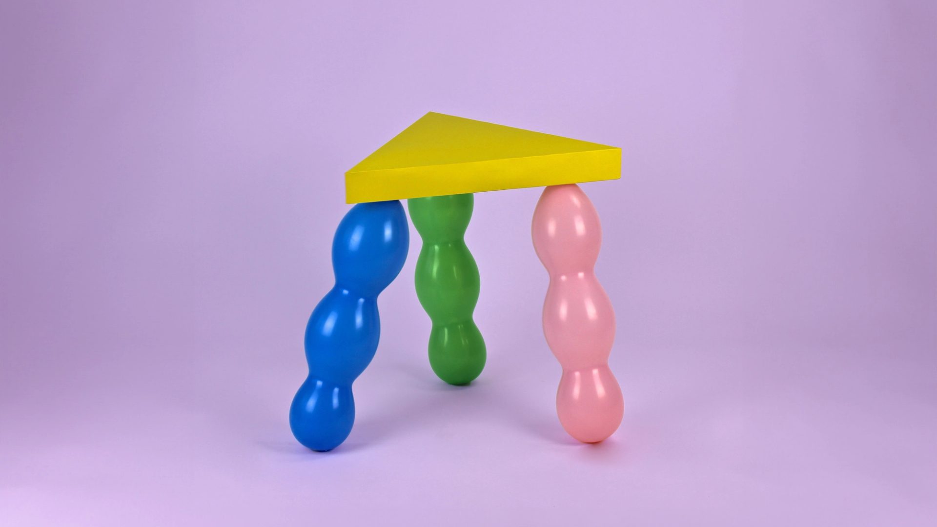 Yellow triangle seat supported by 3 balloon legs in green, pink and blue.