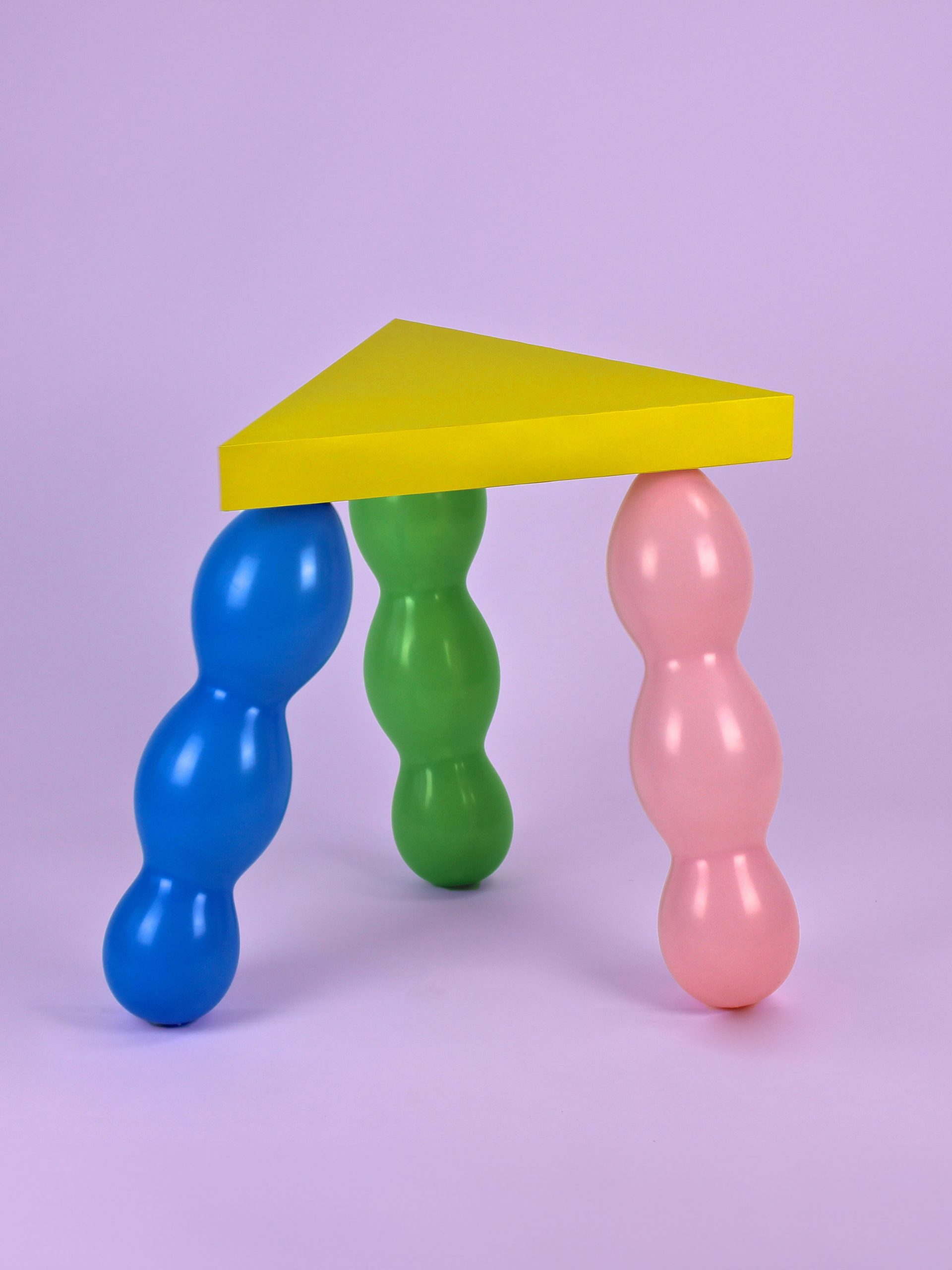 Yellow triangle seat supported by 3 balloon legs in green, pink and blue.