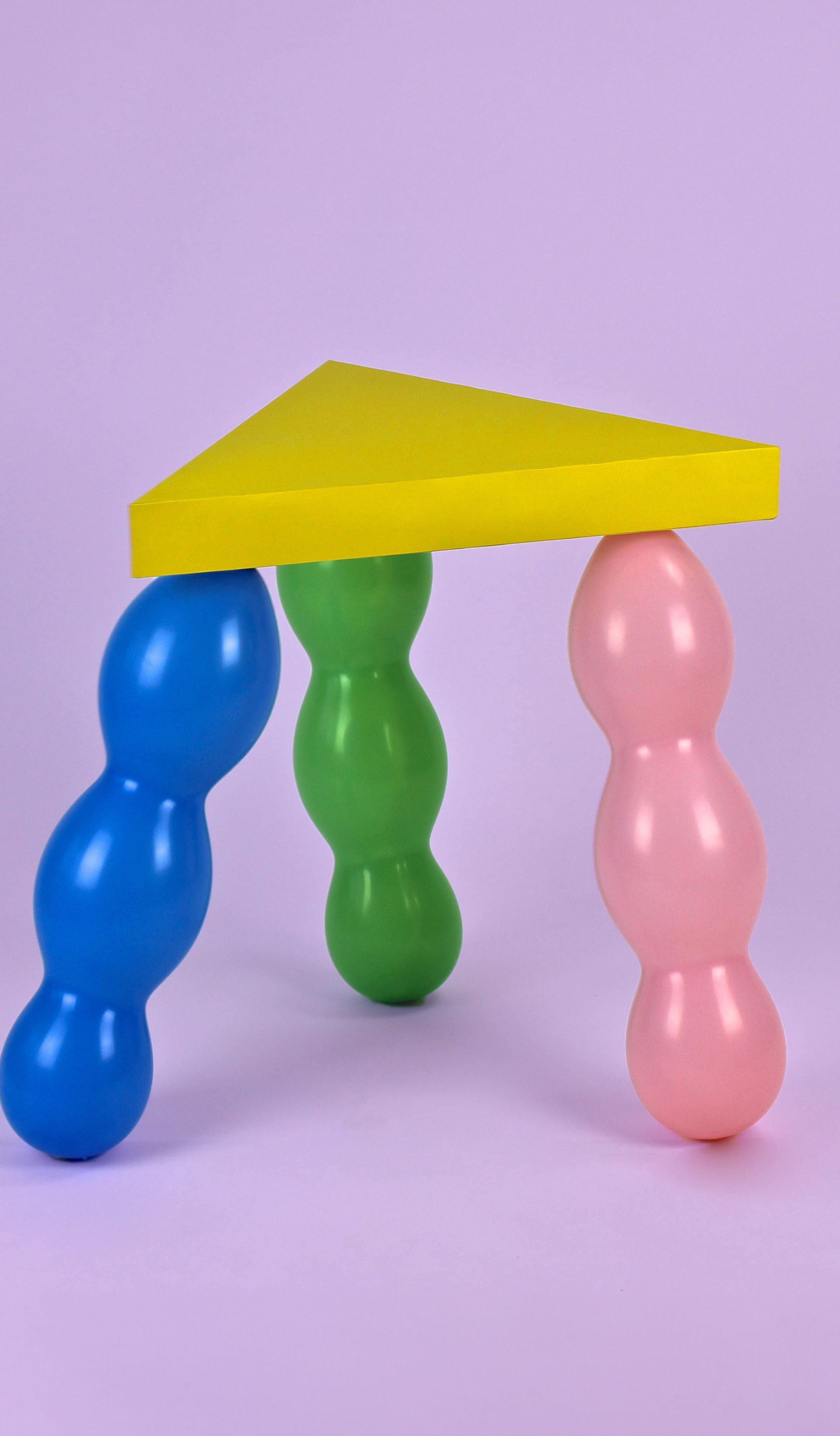 Yellow triangle seat supported by 3 balloon legs in green, pink and blue.