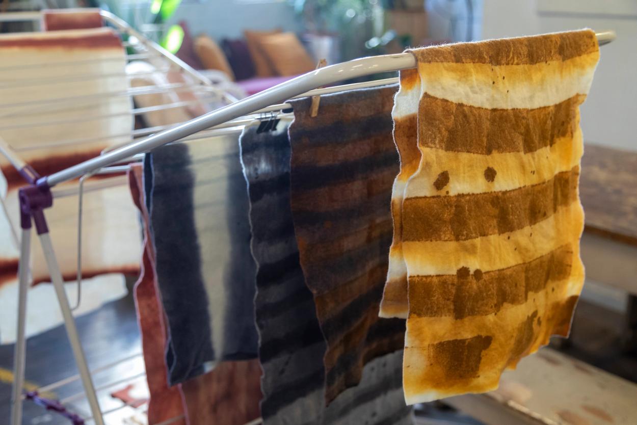 Four textiles, naturally-dyed with different colours and patterns, drying inside on a clothes rack.