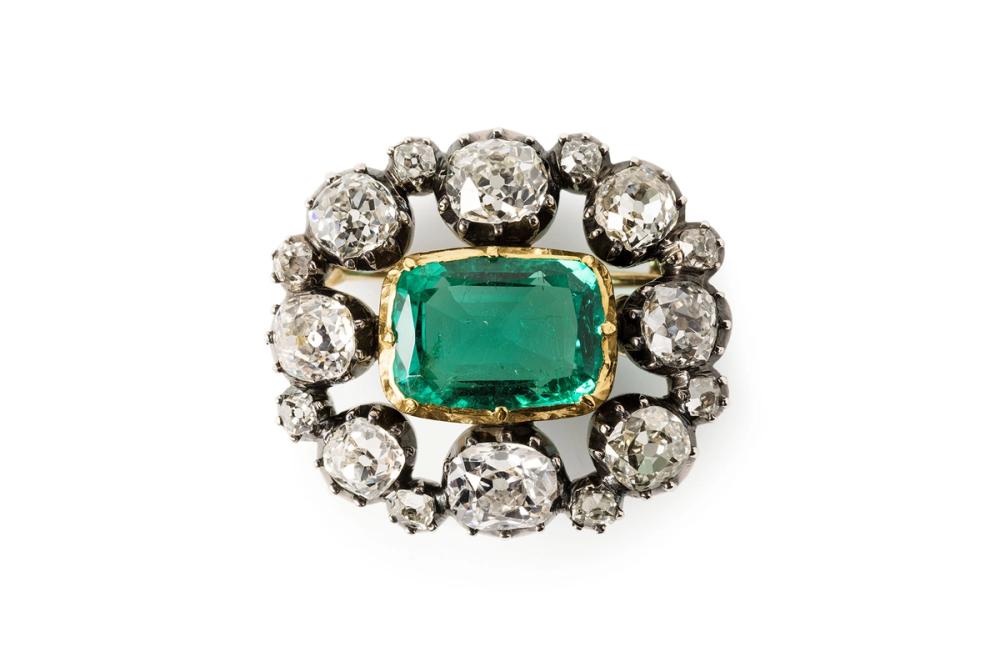 A brooch made of emerald, diamonds, gold and silver with a box made out of leather and wood.