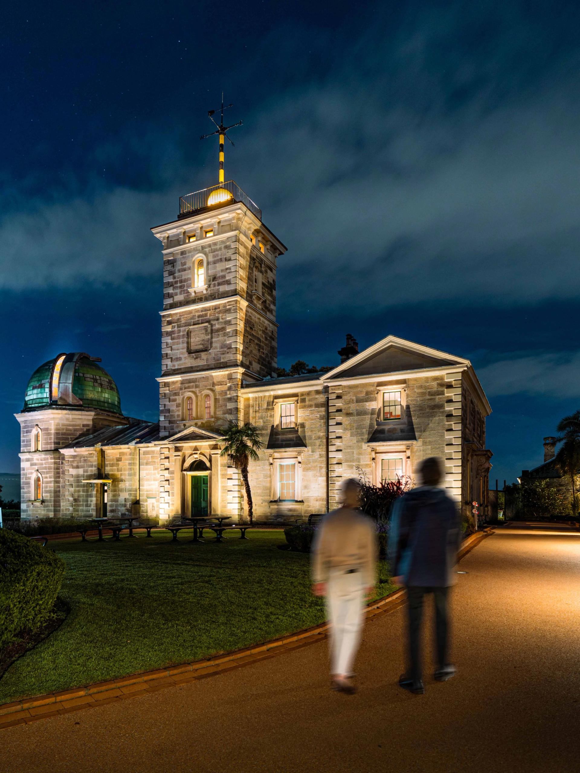 Two people walking down a driveway towards a heritage building.