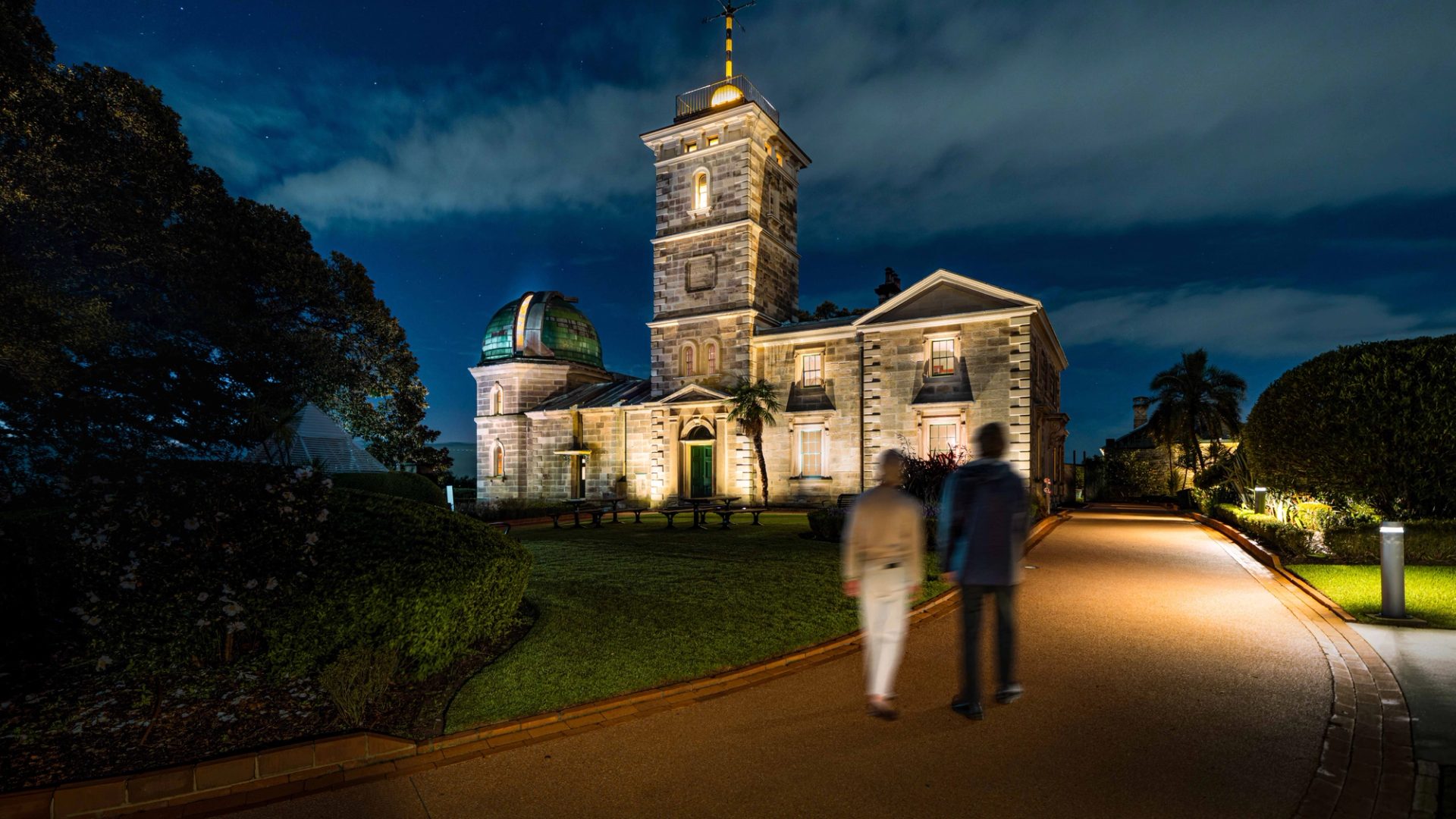 Two people walking down a driveway towards a heritage building.