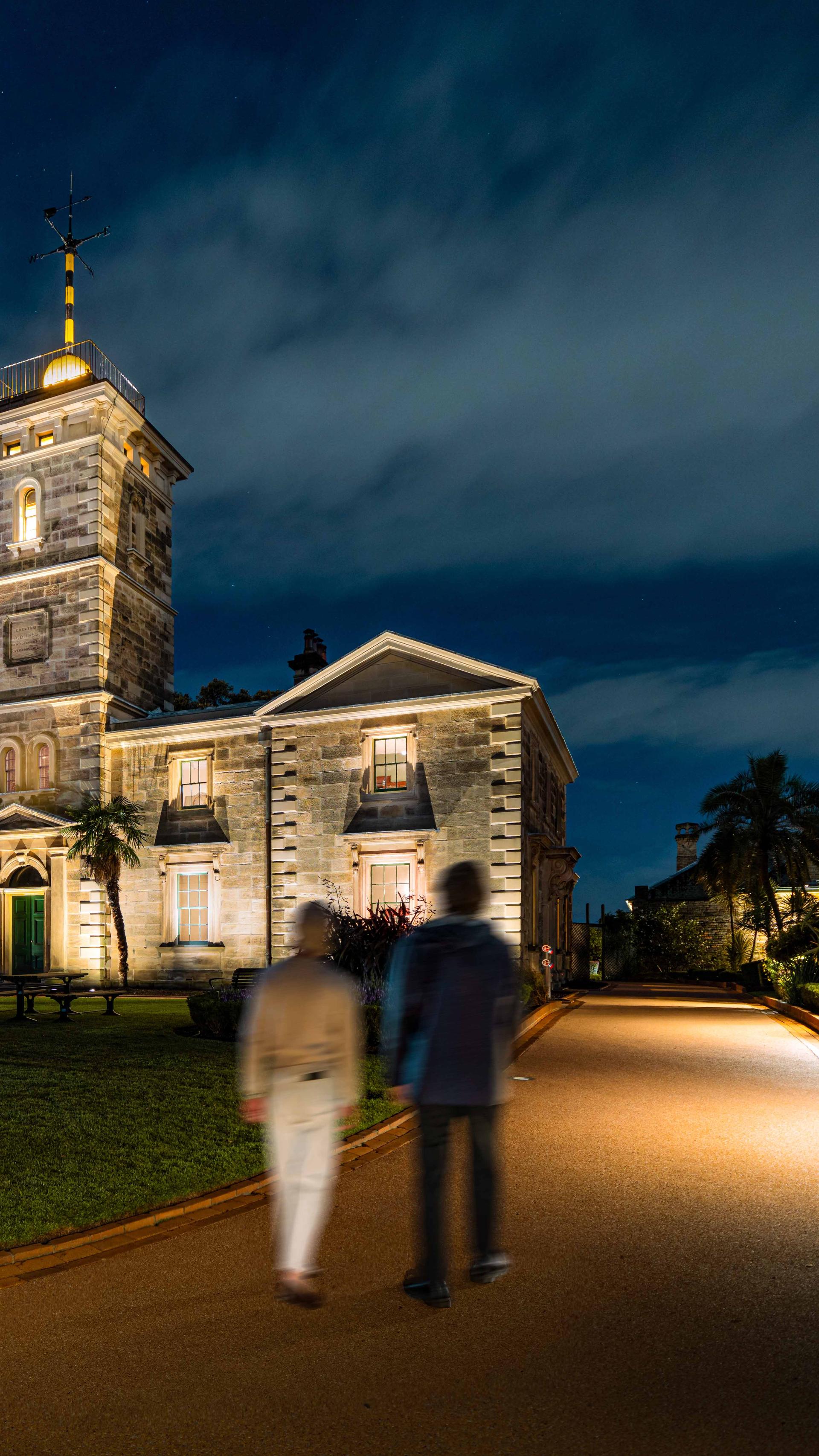 Two people walking down a driveway towards a heritage building.