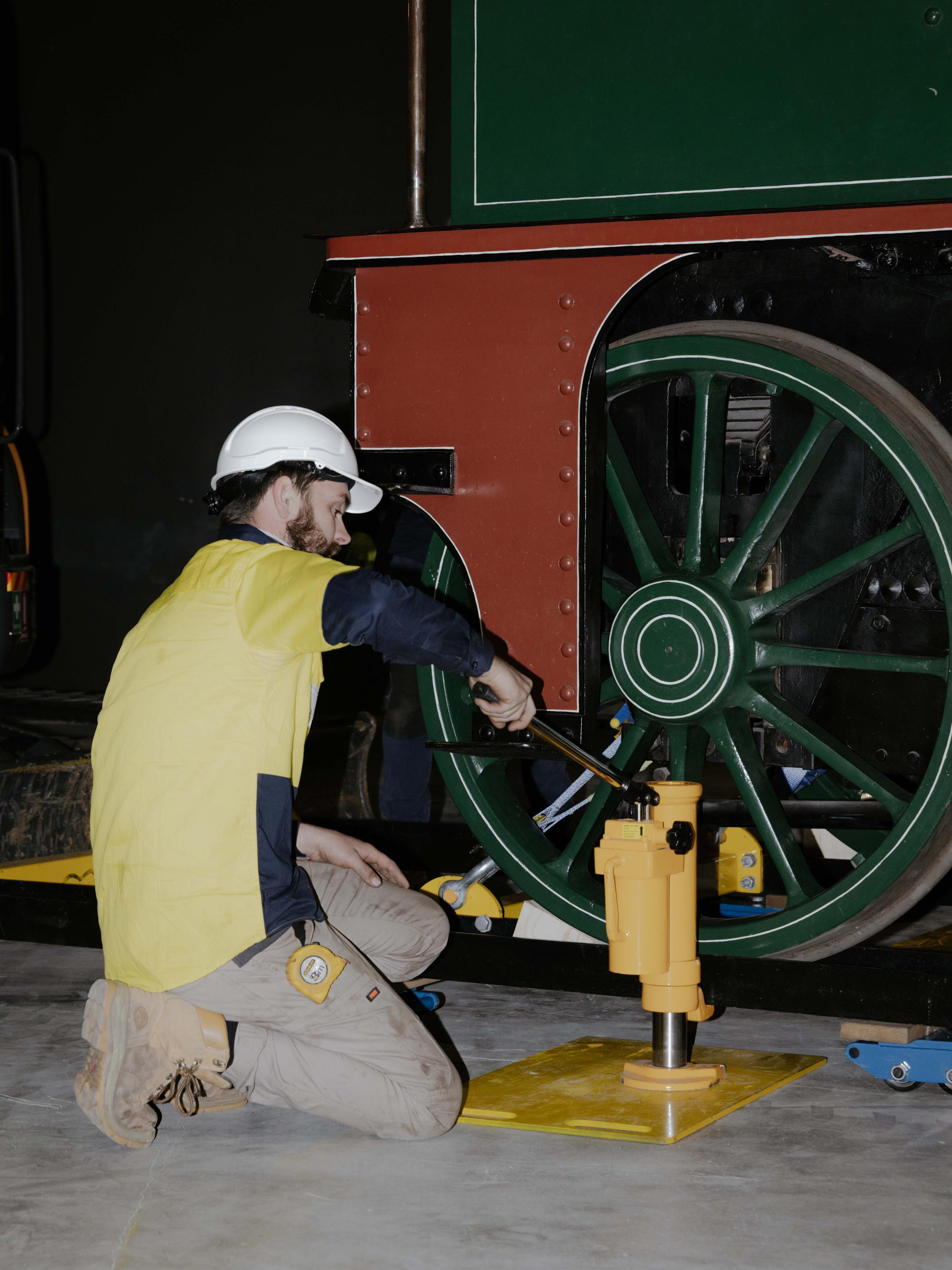 Man pushes down on a yellow vehicle pump next to a train.