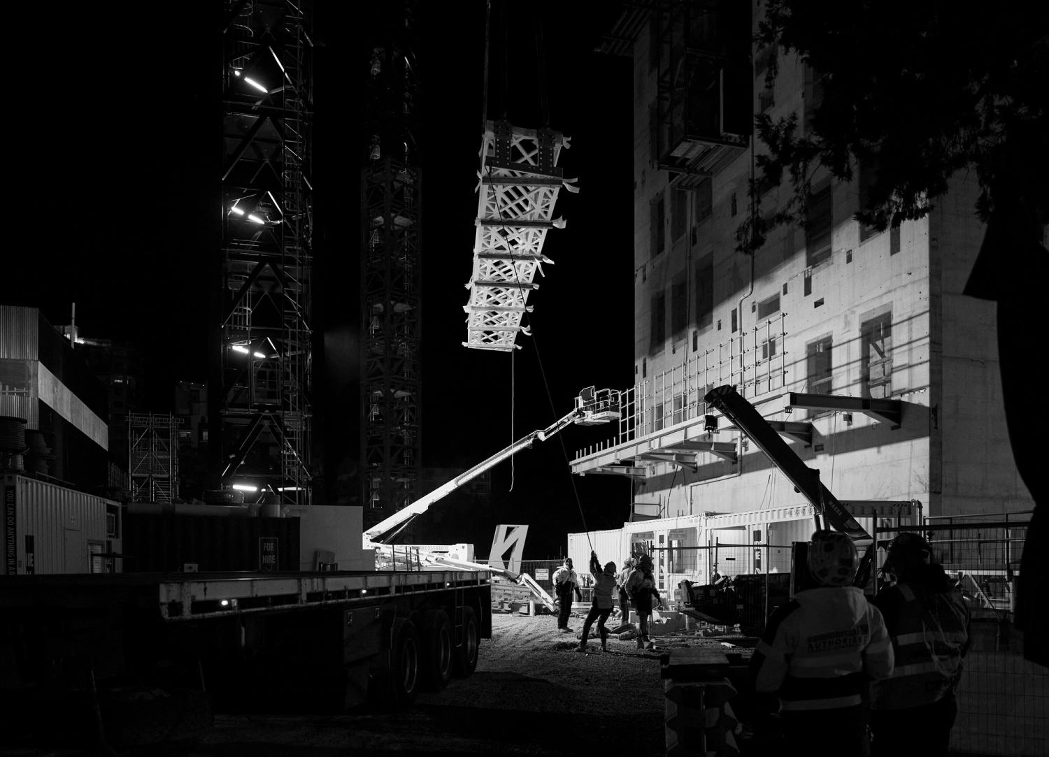 Construction crew working with a crane lifting a heavy frame at night