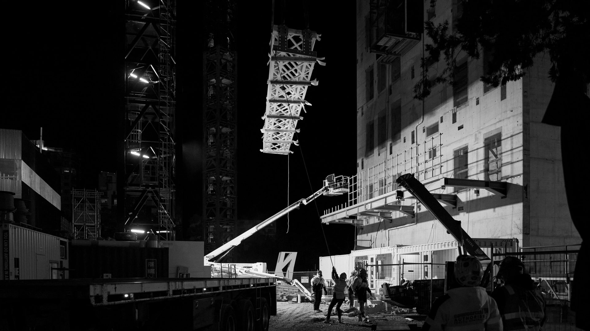 Construction crew working with a crane lifting a heavy frame at night