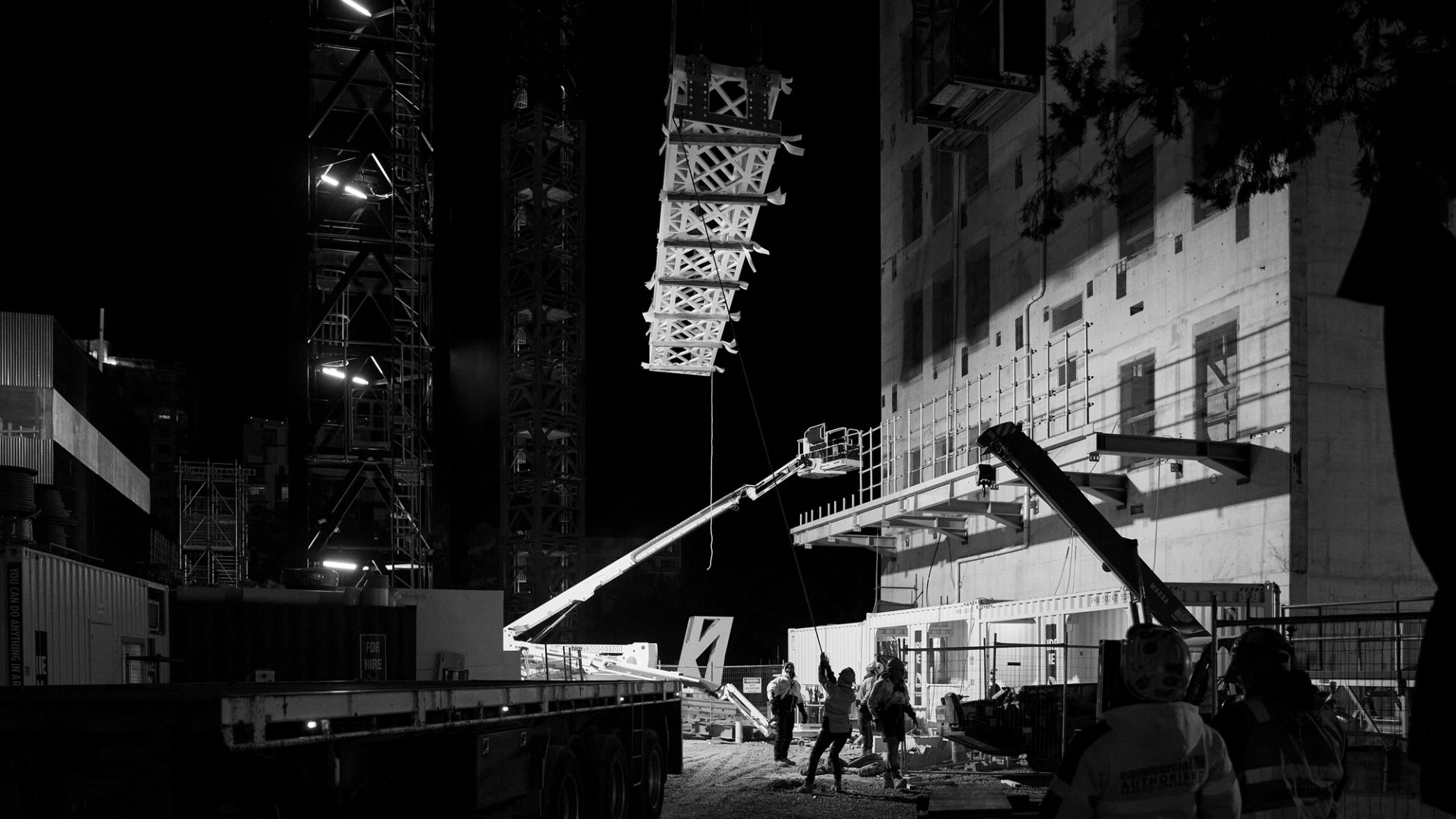 Construction crew working with a crane lifting a heavy frame at night
