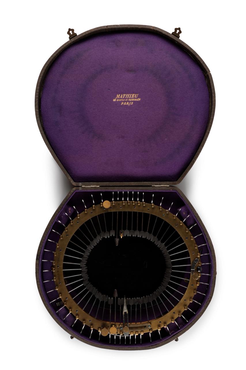 Oval brass frame holding 52 steel spokes (under tension) that are inserted through frame towards centre. The components are held within a wooden box, covered with dark brown leather and lined with purple felt-34cm long. The interior lid is marked in gold writing: Mathieu/113 Boud St Germain/Paris.