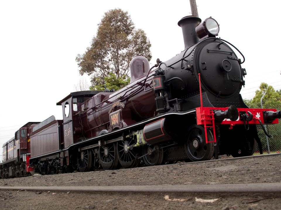 Stationary shiny black locomotive with dark green carriages outside a large brick building with schoolgirls in uniform looking on.