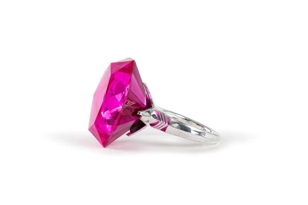 Bangle in form of large ring with an oversized pink coloured faceted plastic jewel in a silvercoated plastic bezel and band.