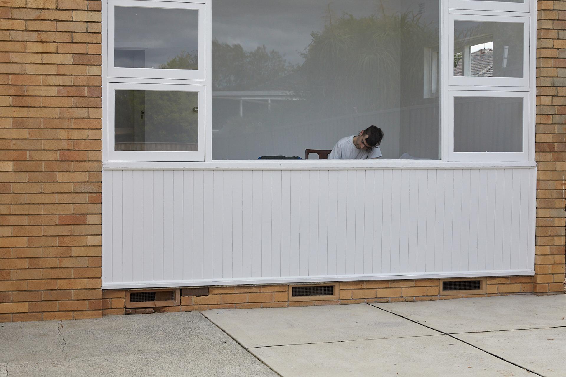 Figure hunched over through the window of a house