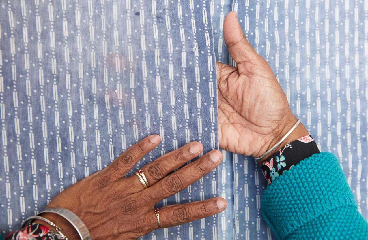 A woman’s brown hands on top and in between the opening of a blue shirt with a white vertical pattern.