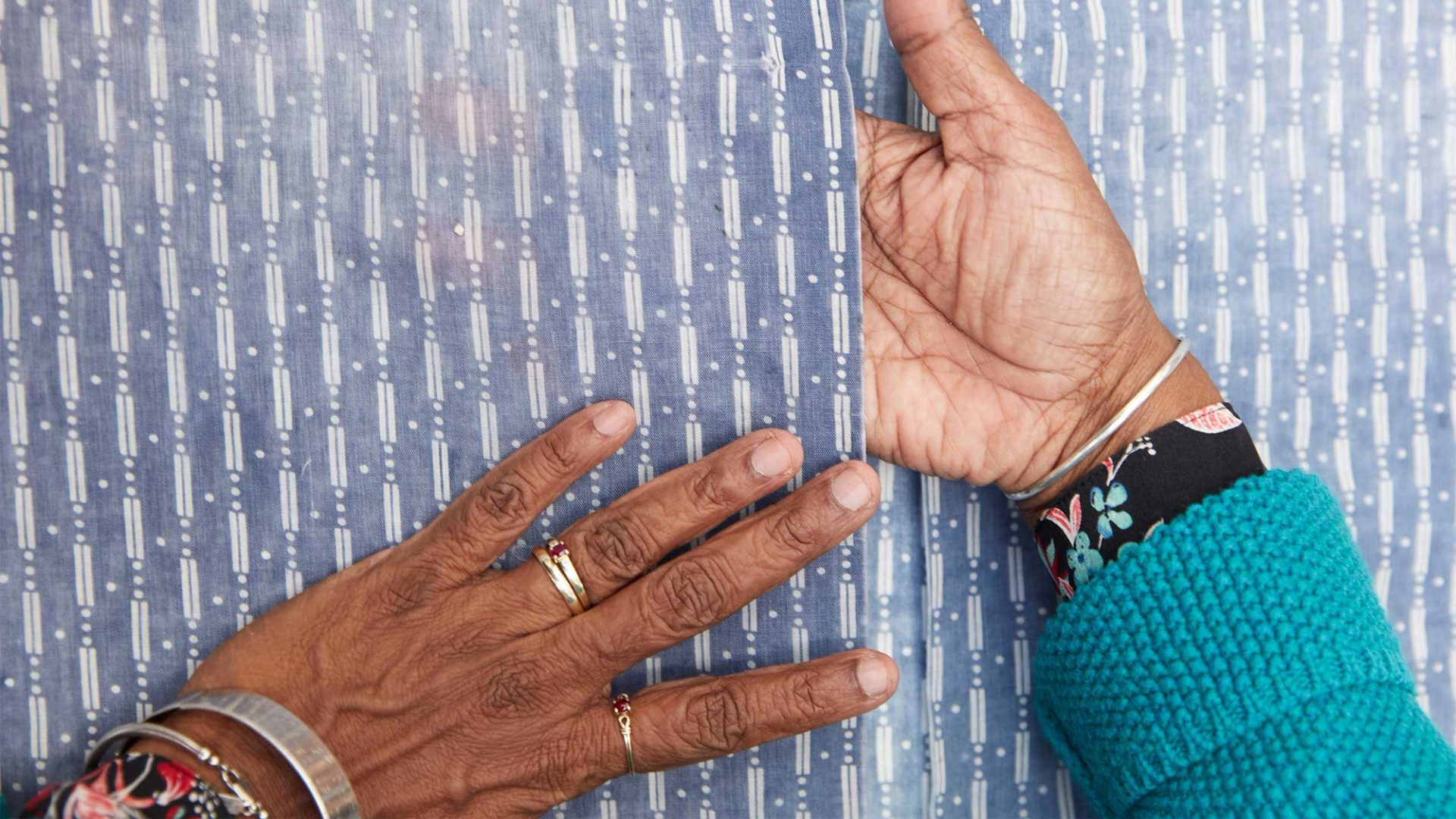 A woman’s brown hands on top and in between the opening of a blue shirt with a white vertical pattern.