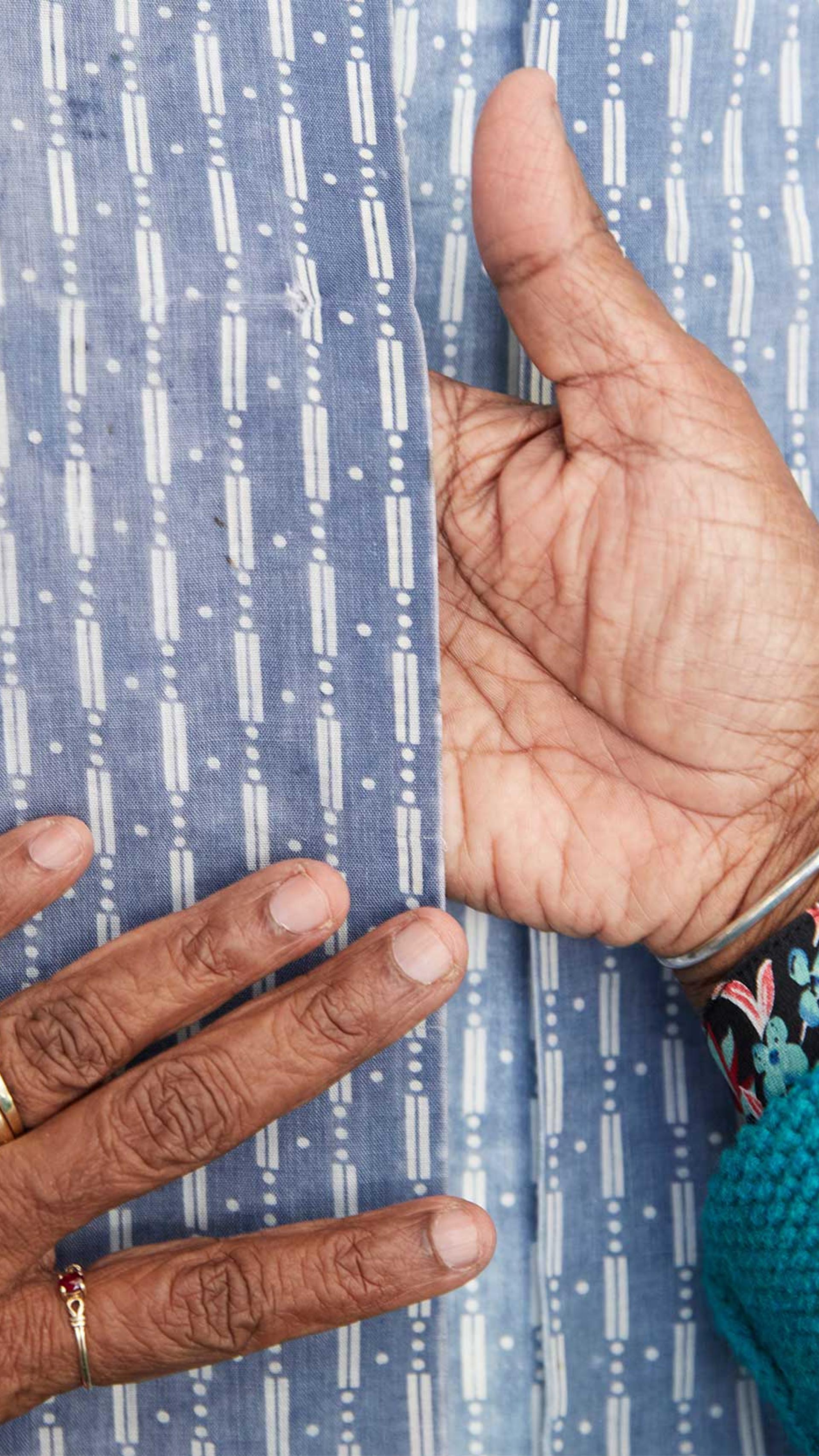 A woman’s brown hands on top and in between the opening of a blue shirt with a white vertical pattern.
