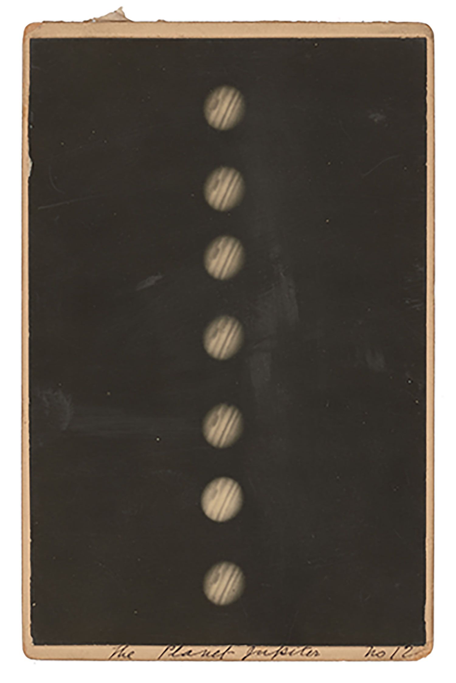 A black and white photograph of Jupiter mounted on a piece of cardboard. The photograph shows several images of Jupiter in a line. The red spot and bands of Jupiter are visible. Handwritten annotations thought to have been made by H C Russell on the mount.