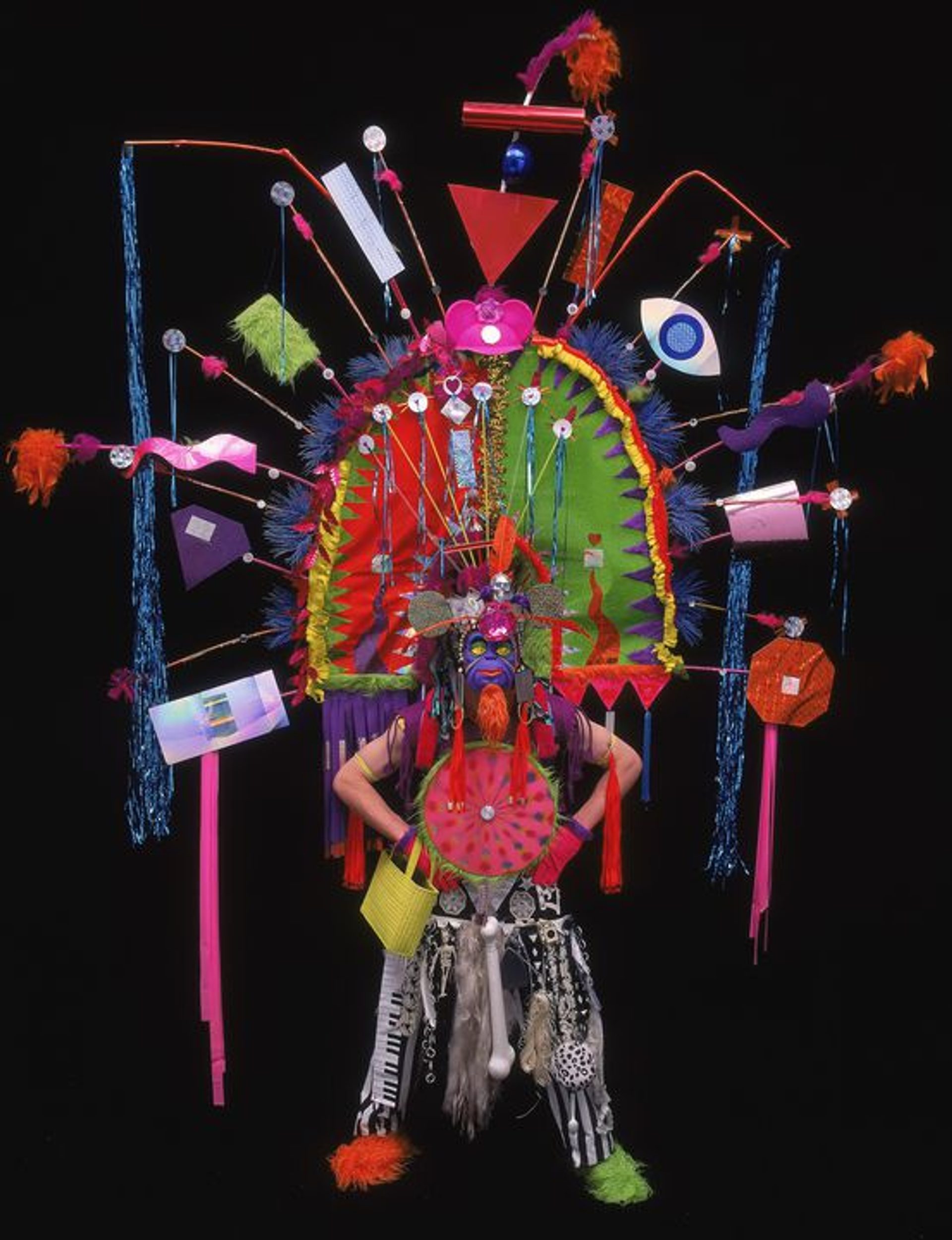 Costume comprising t-shirt, trousers, pair of gloves, pair of overshoes, mask, pair of arm bands, tassel, breastplate, apron skirt, handbag, shoulder piece and oversized headdress.