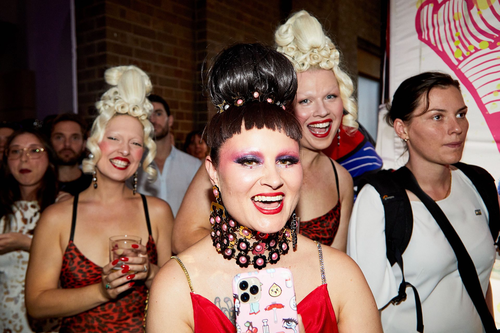 A woman smiles at the camera. She has dark hair in a high bun and is wearing eyeshadow. You can see the top of her red, thin strapped dress.