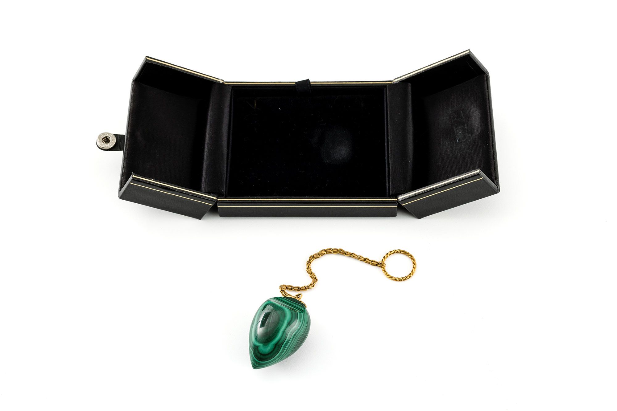 Patterned emerald green and black pendulum with a gold chain in a black velvet box.