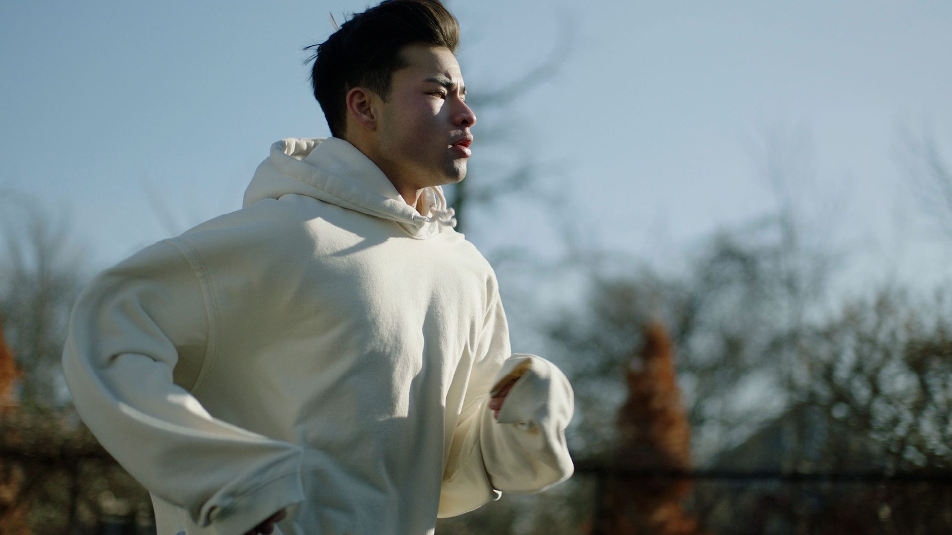 Young adult in a grey hoodie running from the left to right