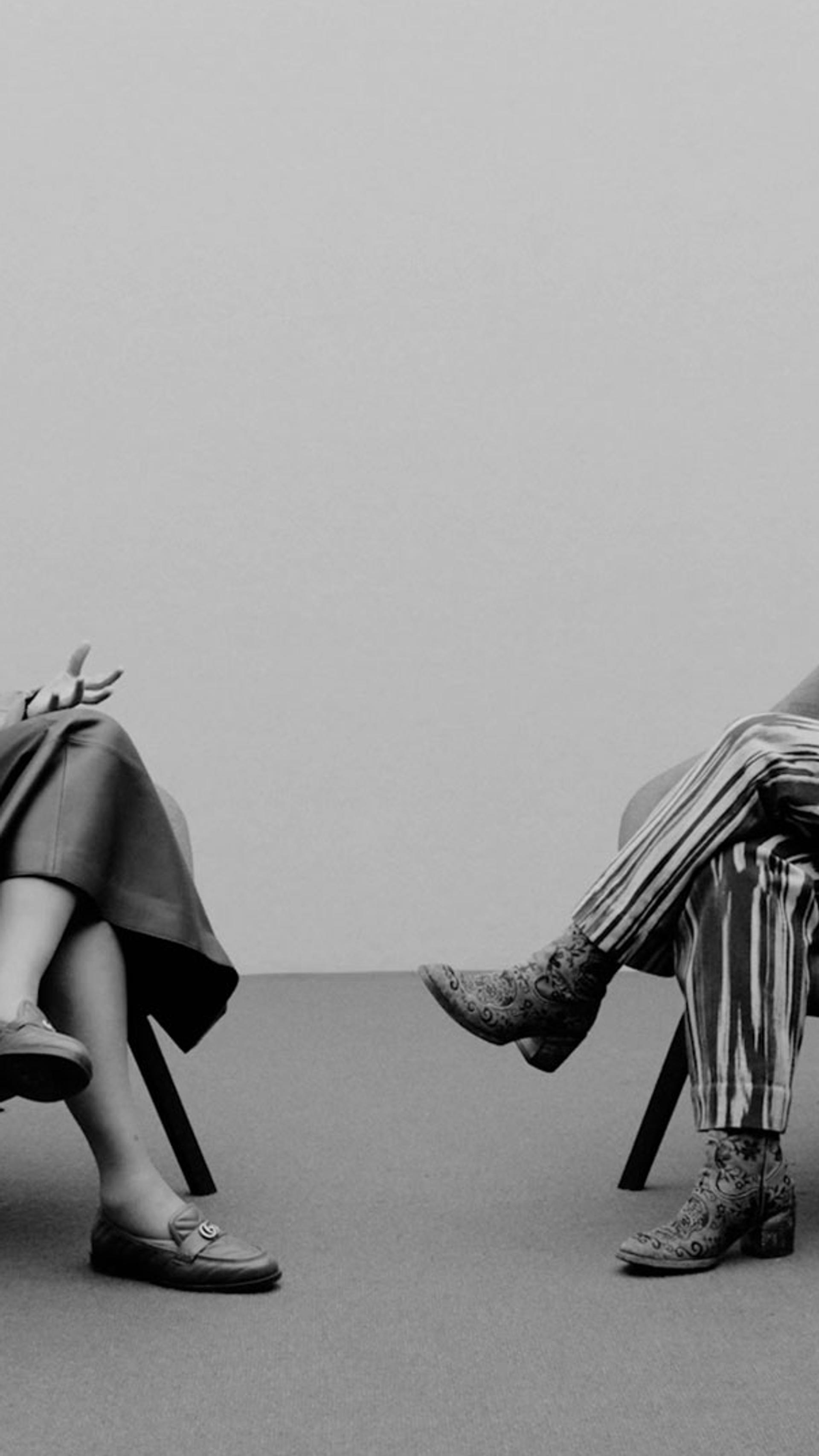 Two women sit on chairs on a stage talking to each other.
