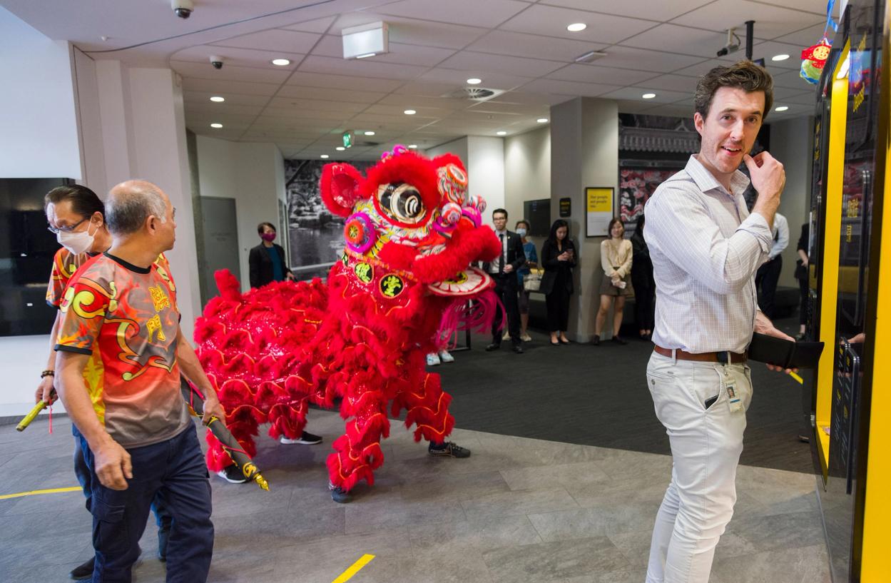 A Lunar New Year lion is in the foyer of a building, a figure in a business shirt smiles in the foreground.