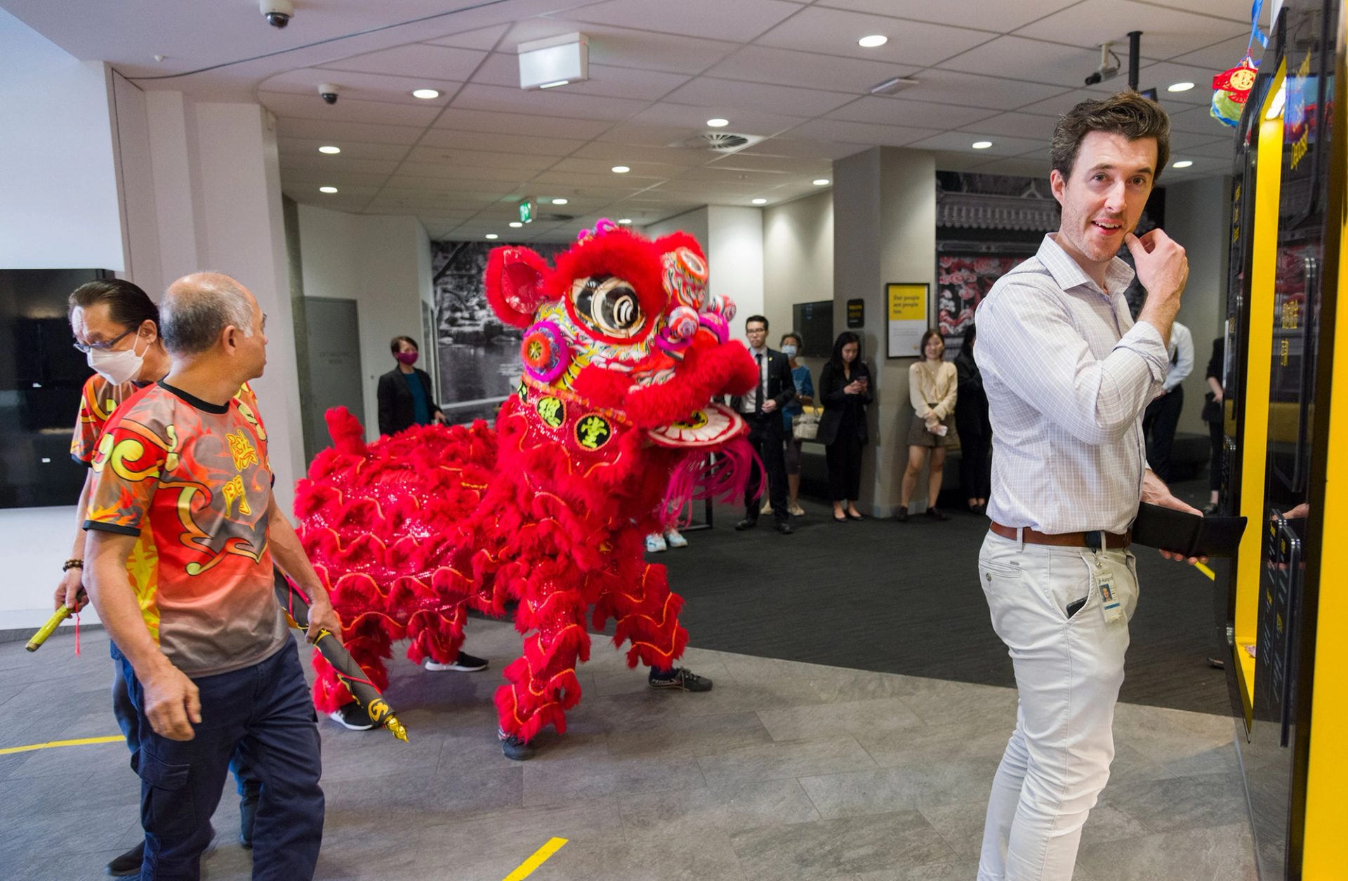 A Lunar New Year lion is in the foyer of a building, a figure in a business shirt smiles in the foreground.