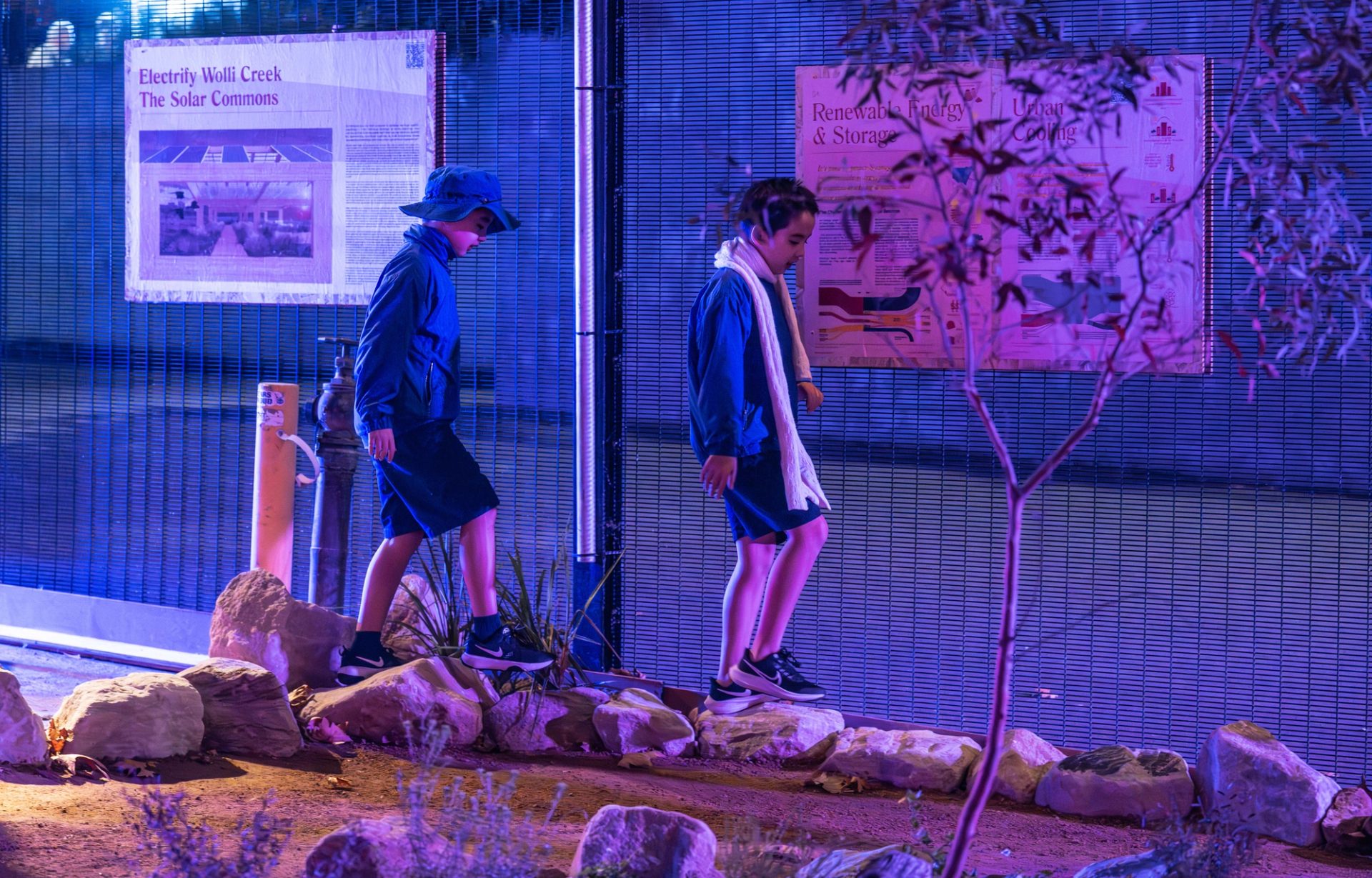 Two children stepping on stones in a garden at night, lit by cool toned lighting.