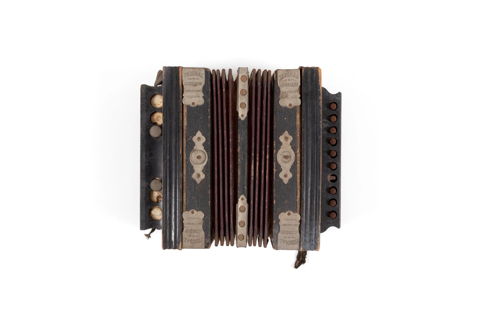 Small musical accordion made from leather, black-painted wood, metal, paper and fabric. Above the keys is the text: "Federal". Metal reinforcing plates on each corner are stamped with the text: "FEDERAL / ACCORDION / MADE IN GERMANY / REGISTERED"