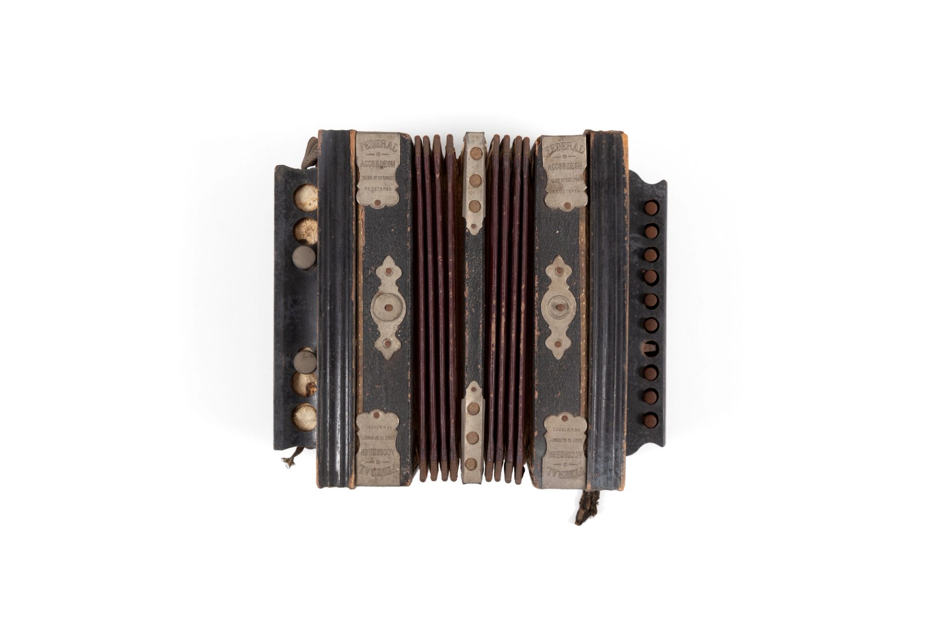 Small musical accordion made from leather, black-painted wood, metal, paper and fabric. Above the keys is the text: "Federal". Metal reinforcing plates on each corner are stamped with the text: "FEDERAL / ACCORDION / MADE IN GERMANY / REGISTERED"