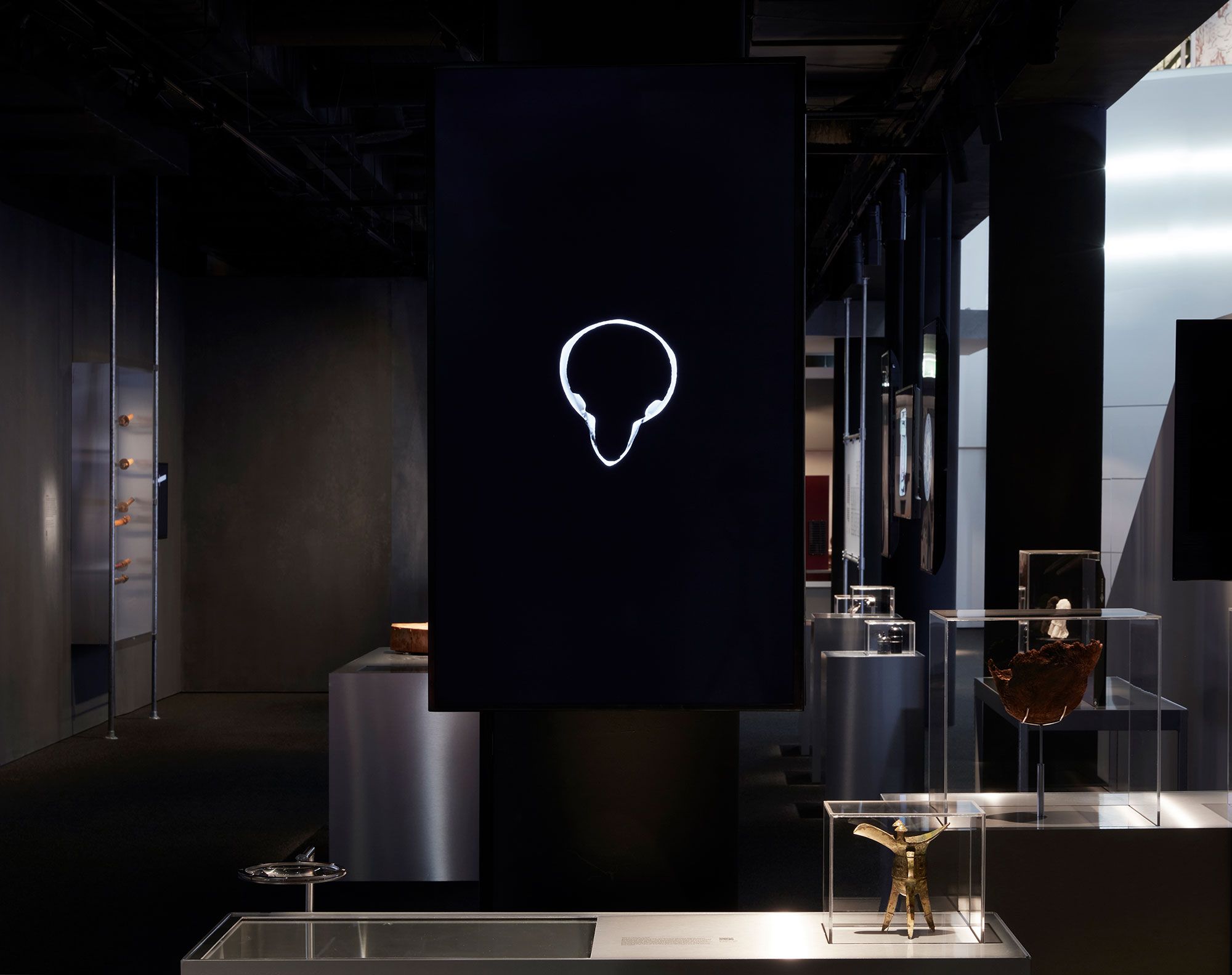 An exhibition view a dark space containing a series of stainless steel plinths and perspex cases.