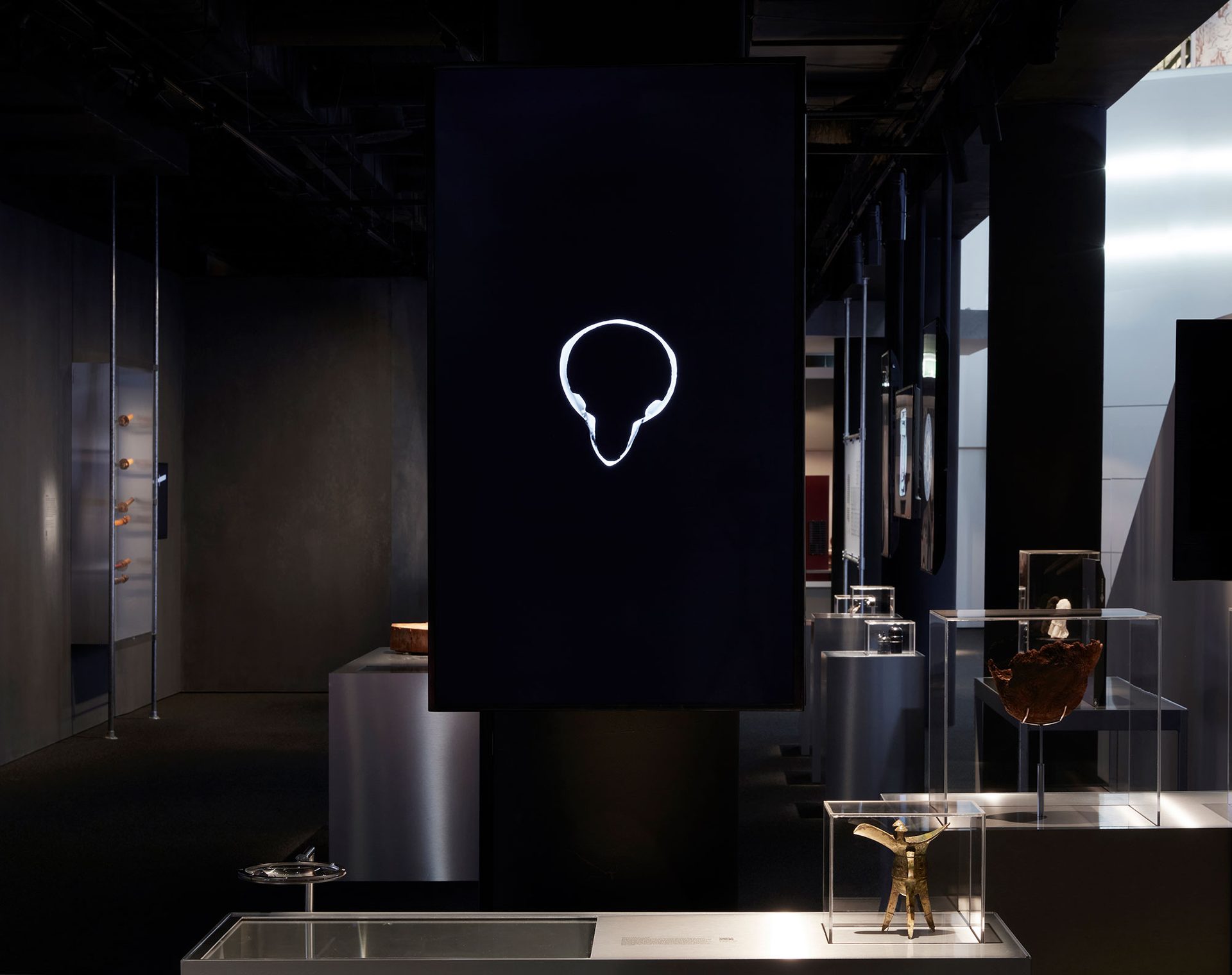 An exhibition view a dark space containing a series of stainless steel plinths and perspex cases.